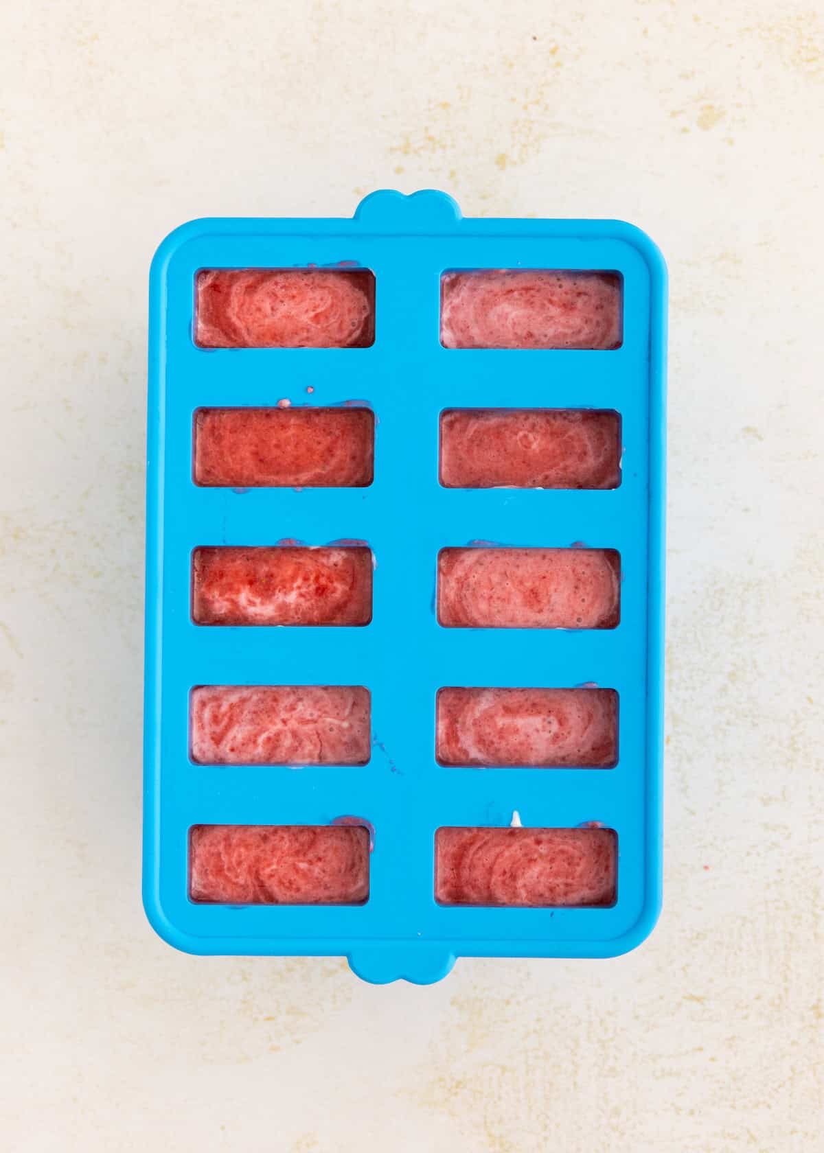 Blue silicone mold filled with a pink-red frozen mixture on a light surface.