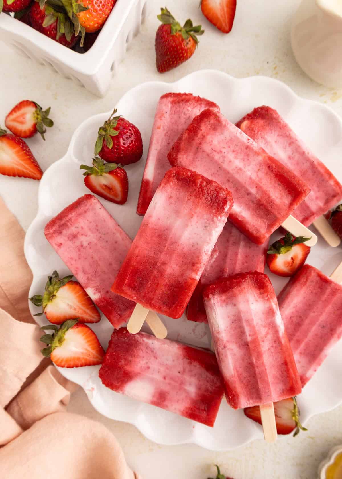 Strawberry popsicles on a white plate with fresh strawberries scattered around.