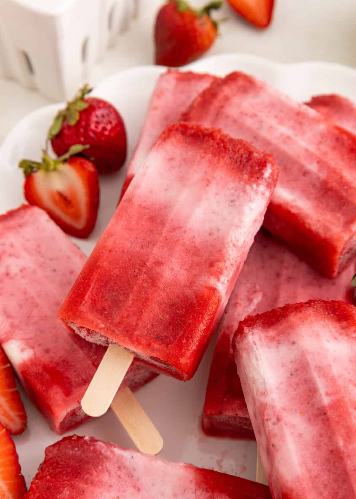 Strawberry popsicles on a plate with fresh strawberries and slices around them.