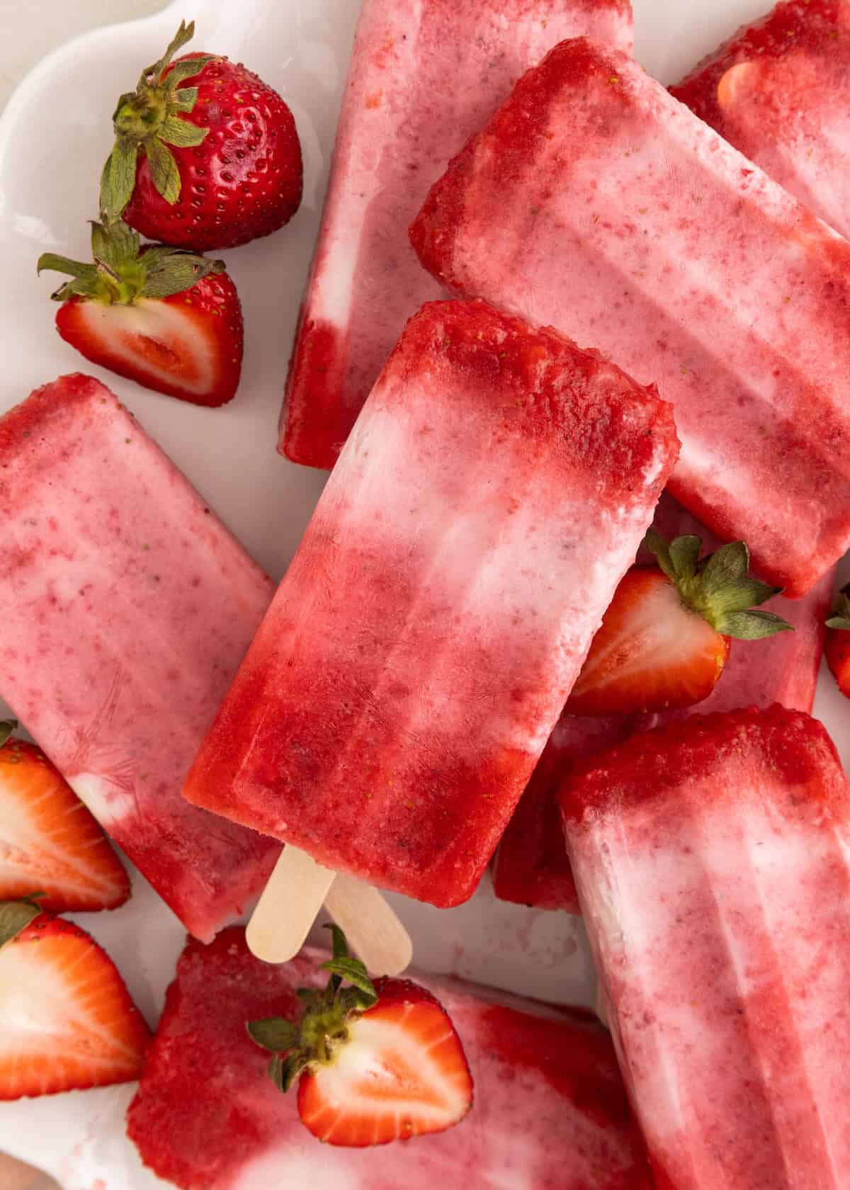 Strawberry popsicles with fresh strawberries on a white plate.