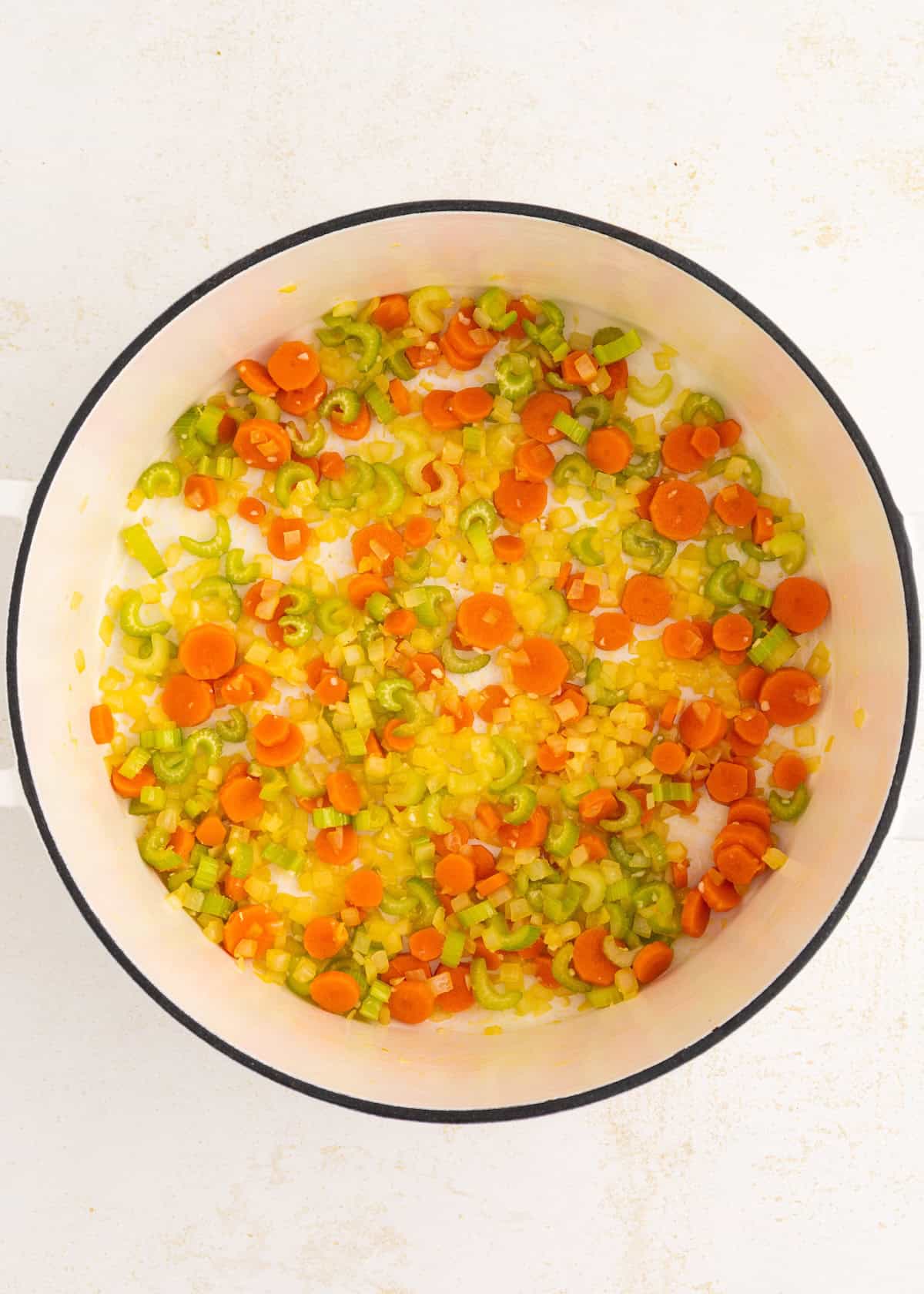 Chopped carrots, celery, and onions sautéing in a white pot.
