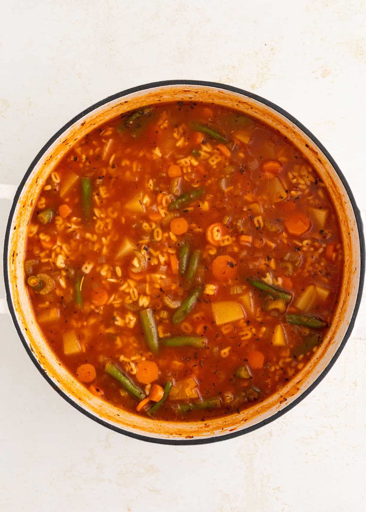 A pot of vegetable soup with pasta, carrots, green beans, and tomato broth.