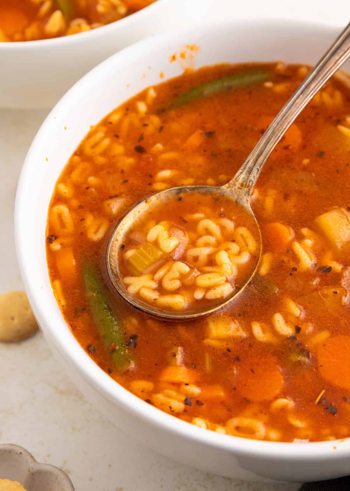 Bowl of alphabet soup with vegetables and a spoon scooping some up.