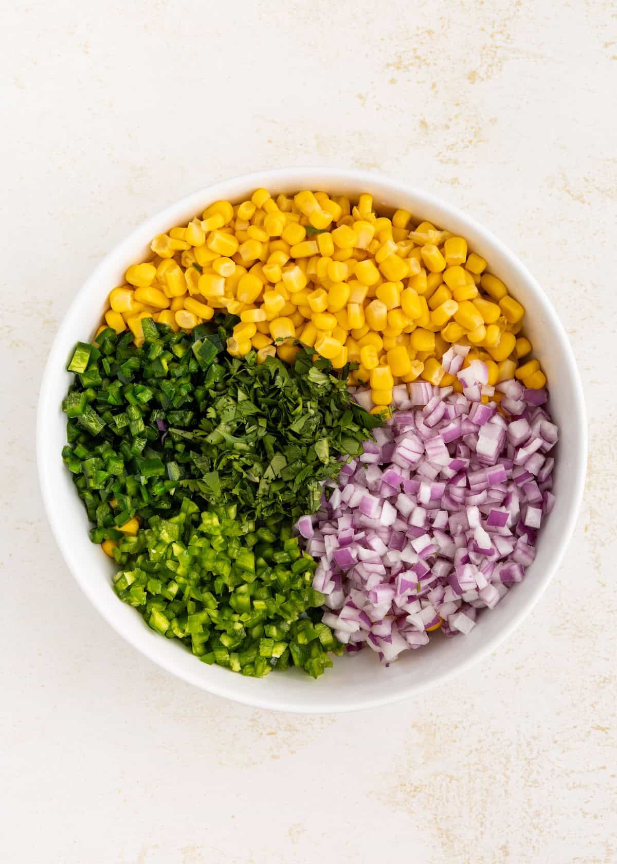 A bowl with corn, chopped jalapeños, red onion, and cilantro, arranged in sections.