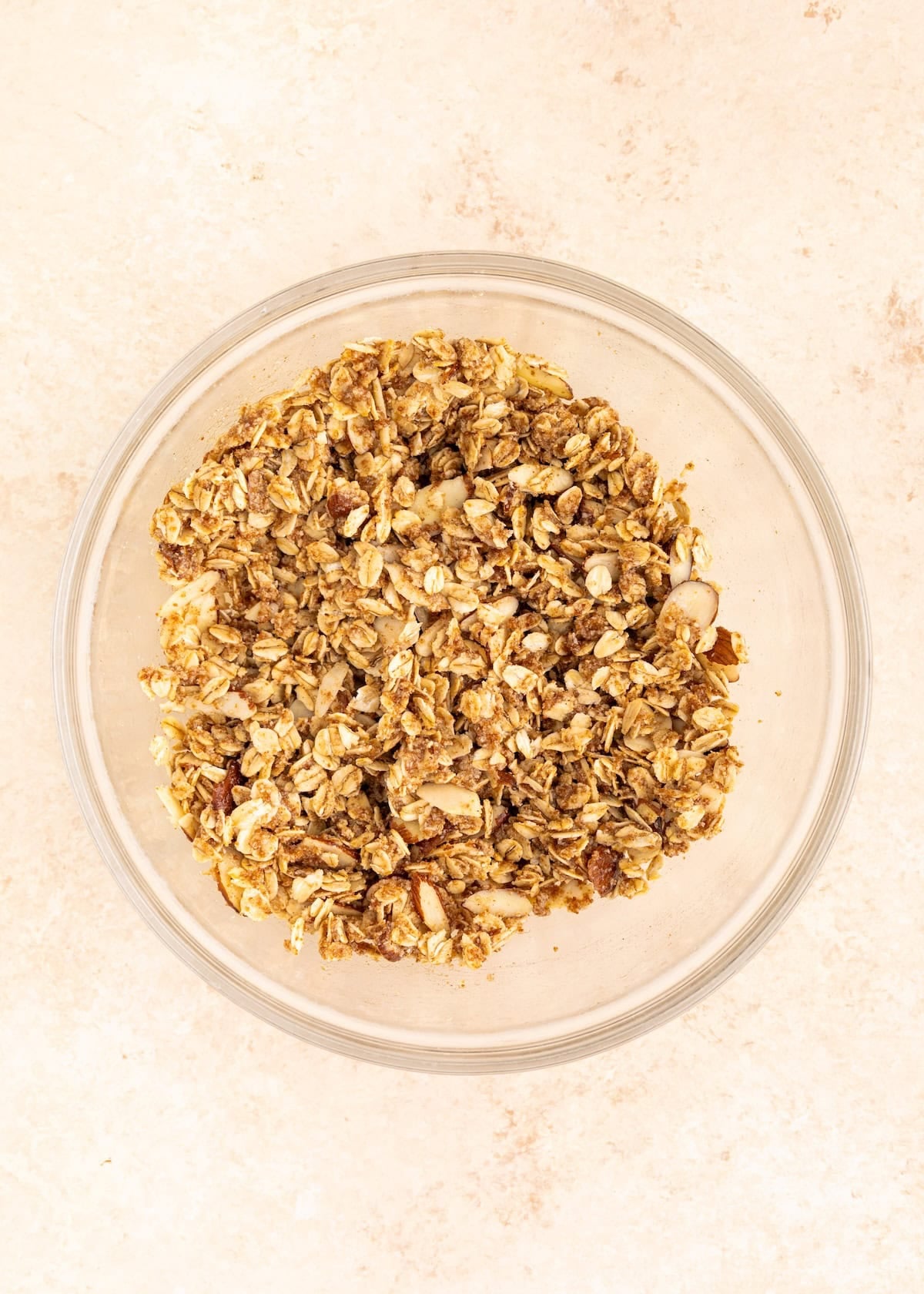 A clear bowl filled with granola on a light beige surface.