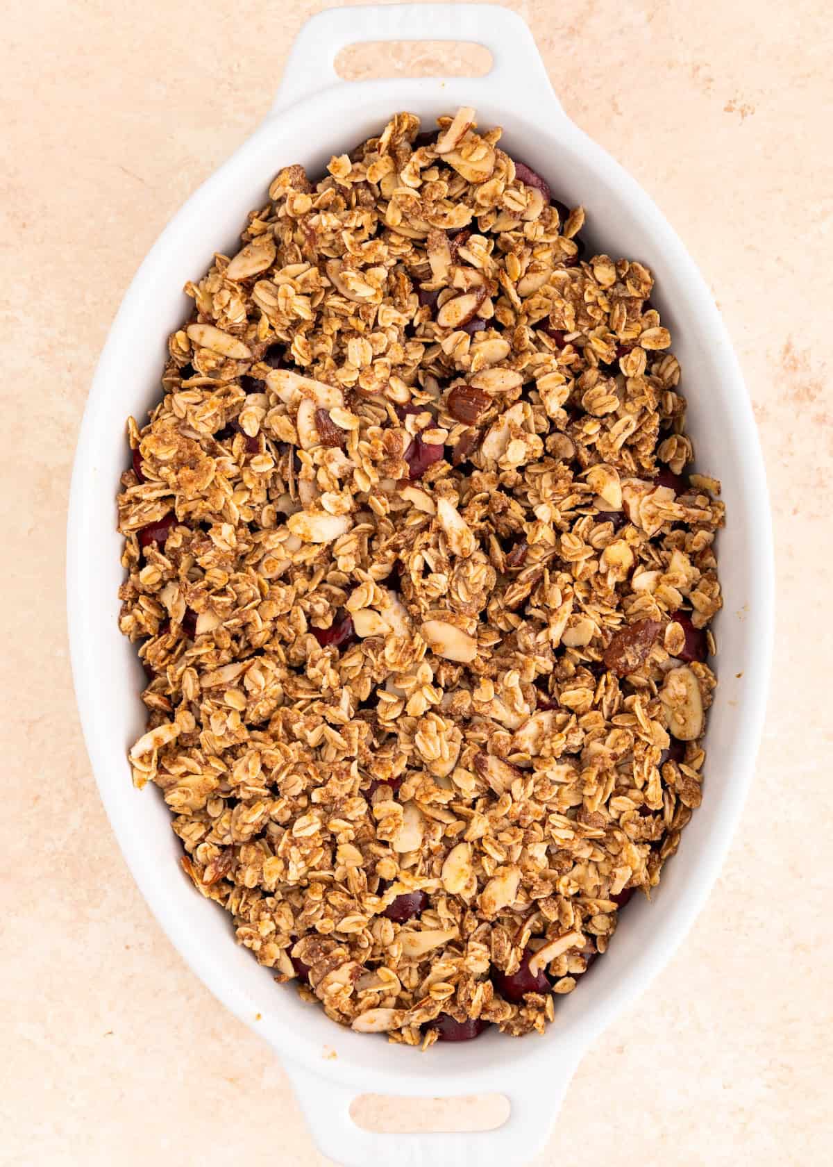 Oval white dish filled with golden brown baked granola topping on a light surface.