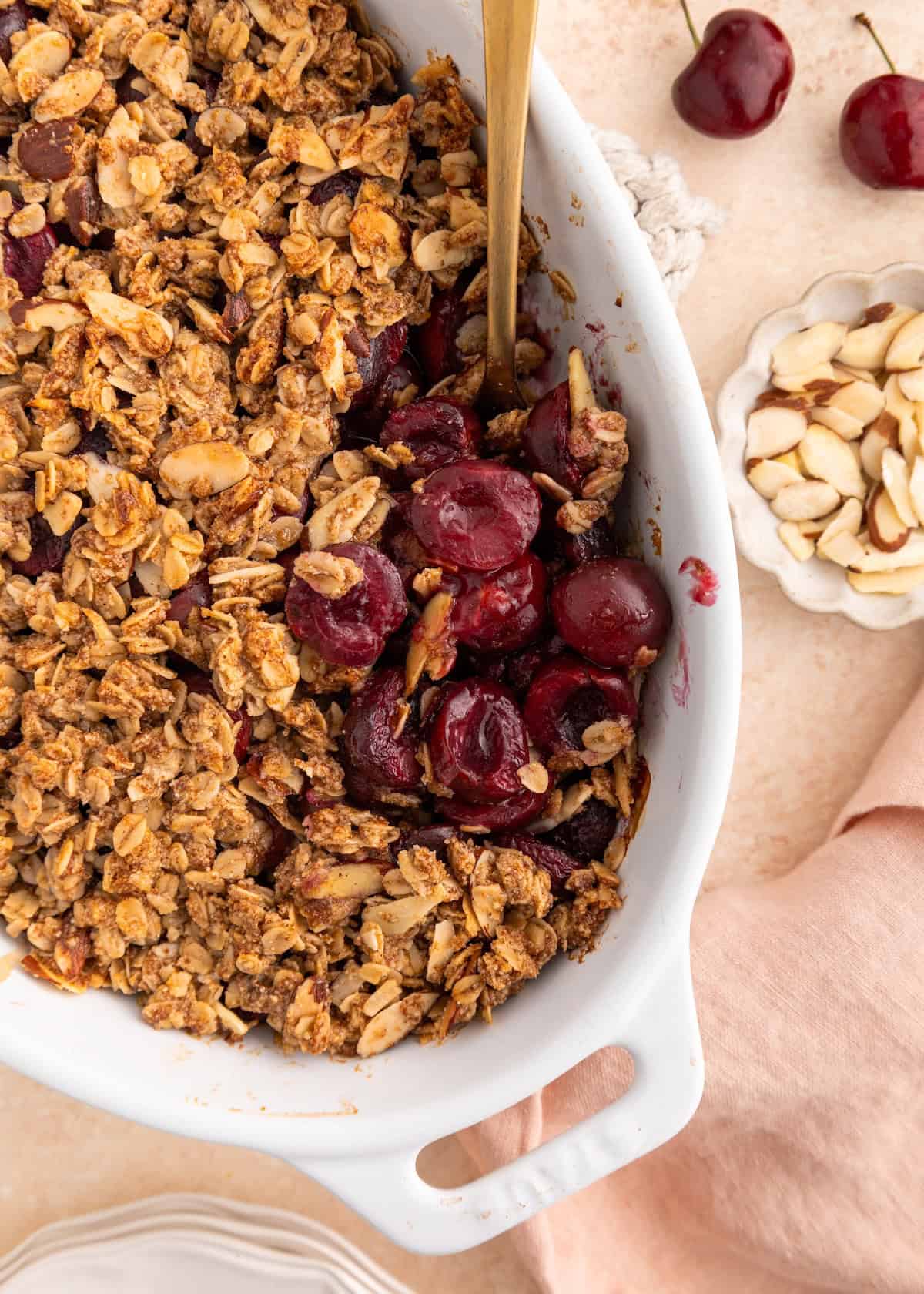 Cherry crumble with oats and almonds in a white baking dish, served with a spoon.