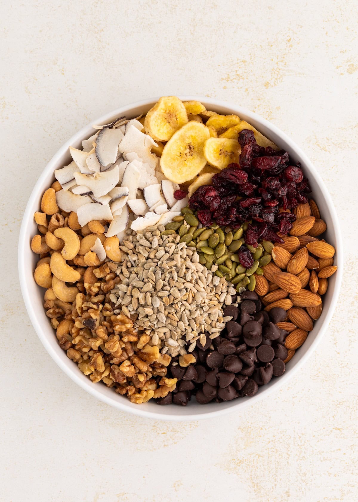 A bowl filled with assorted nuts, seeds, dried fruit, banana chips, and chocolate chips.