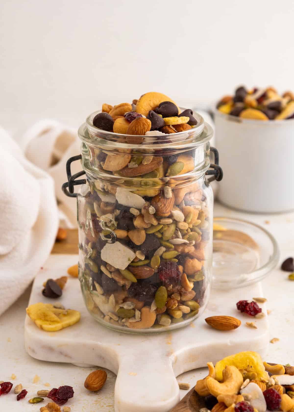 A glass jar filled with mixed nuts, seeds, and chocolate chips on a marble board.
