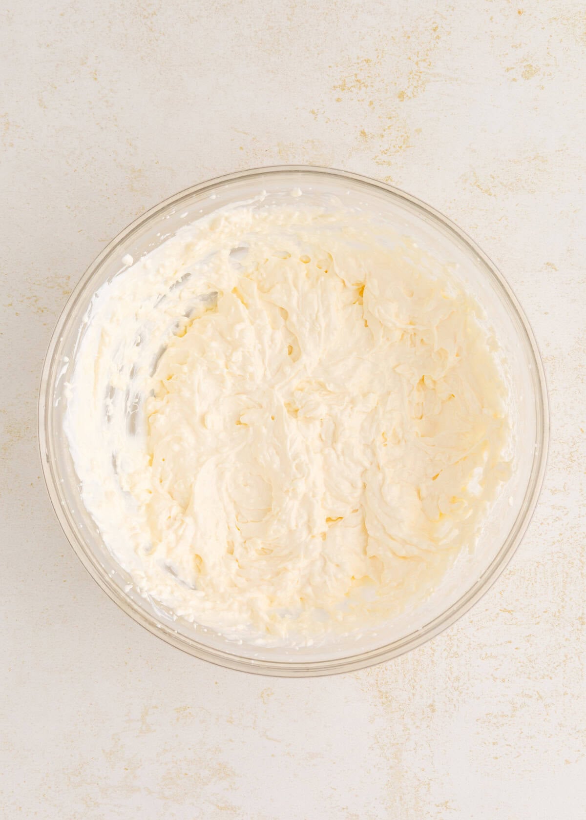 A glass bowl filled with creamy, whipped mixture on a light countertop.