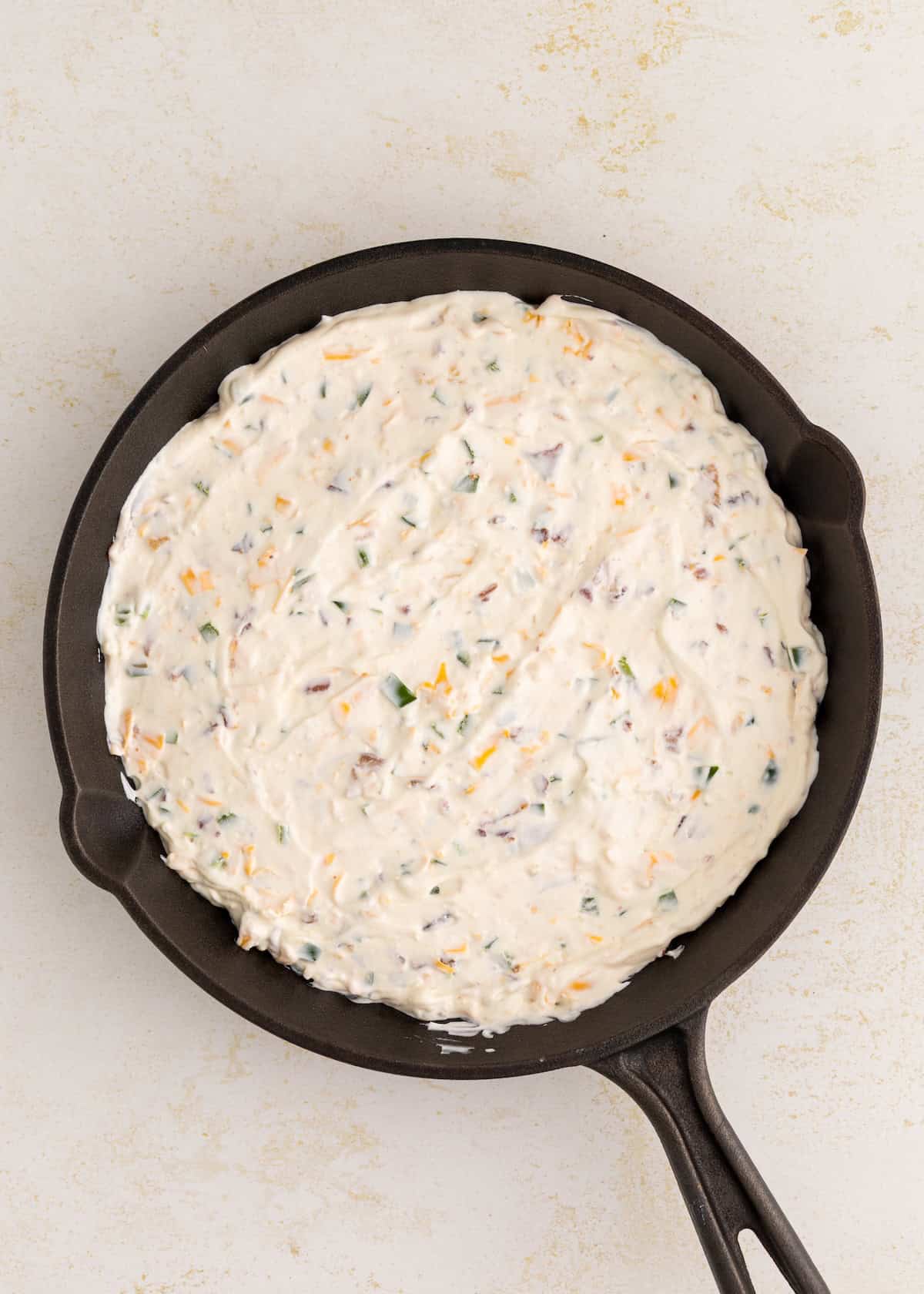 Unbaked cheesy biscuit dough spread in a black cast iron skillet on a light surface.