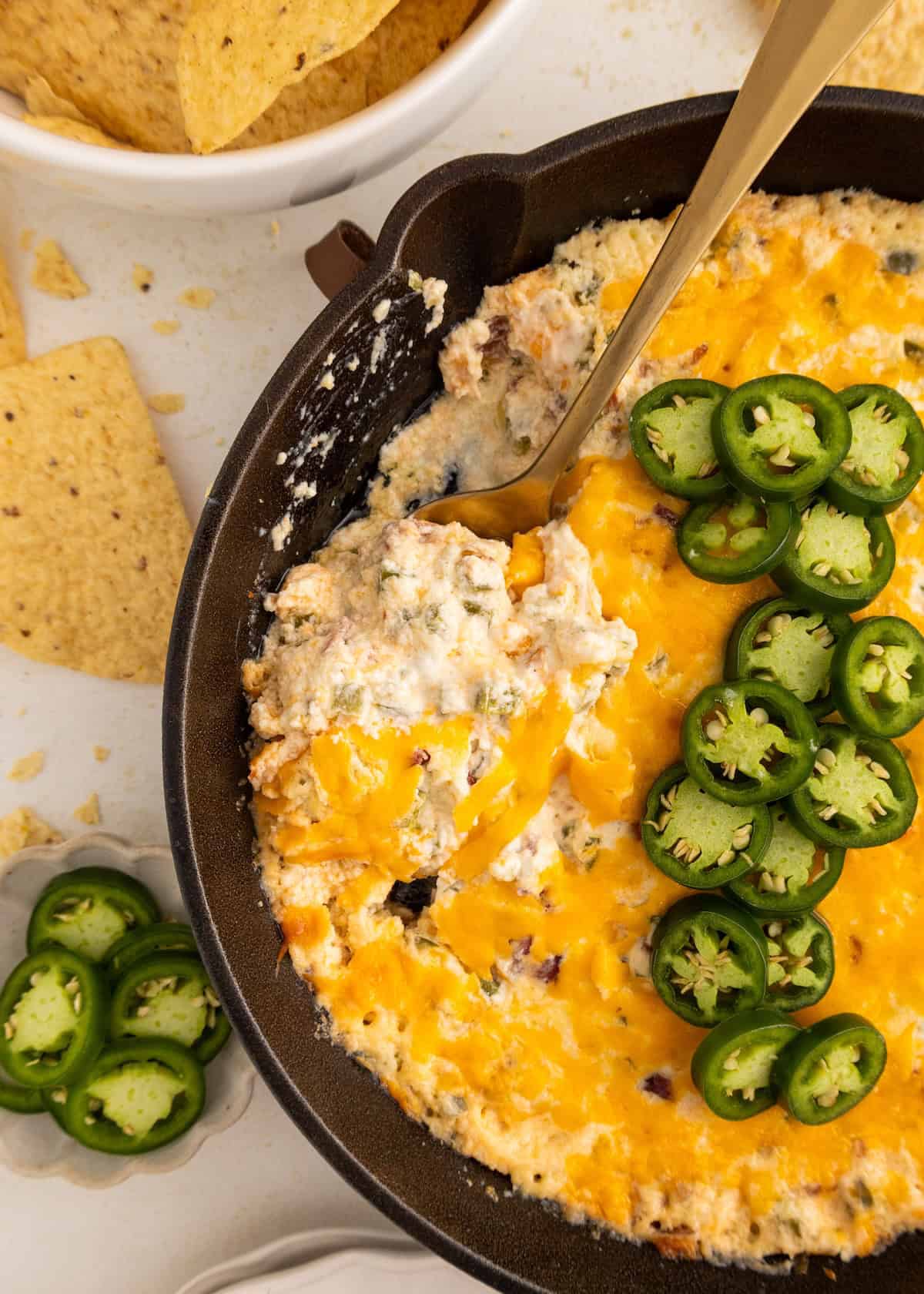 Cheesy baked dip in a skillet topped with sliced jalapeños, with tortilla chips nearby.