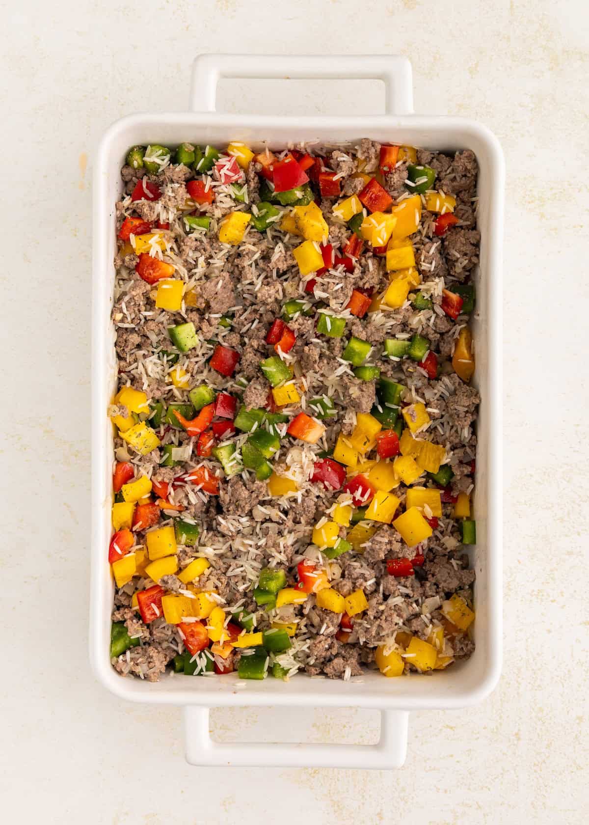 A casserole dish with ground beef, rice, and chopped red, yellow, and green bell peppers.
