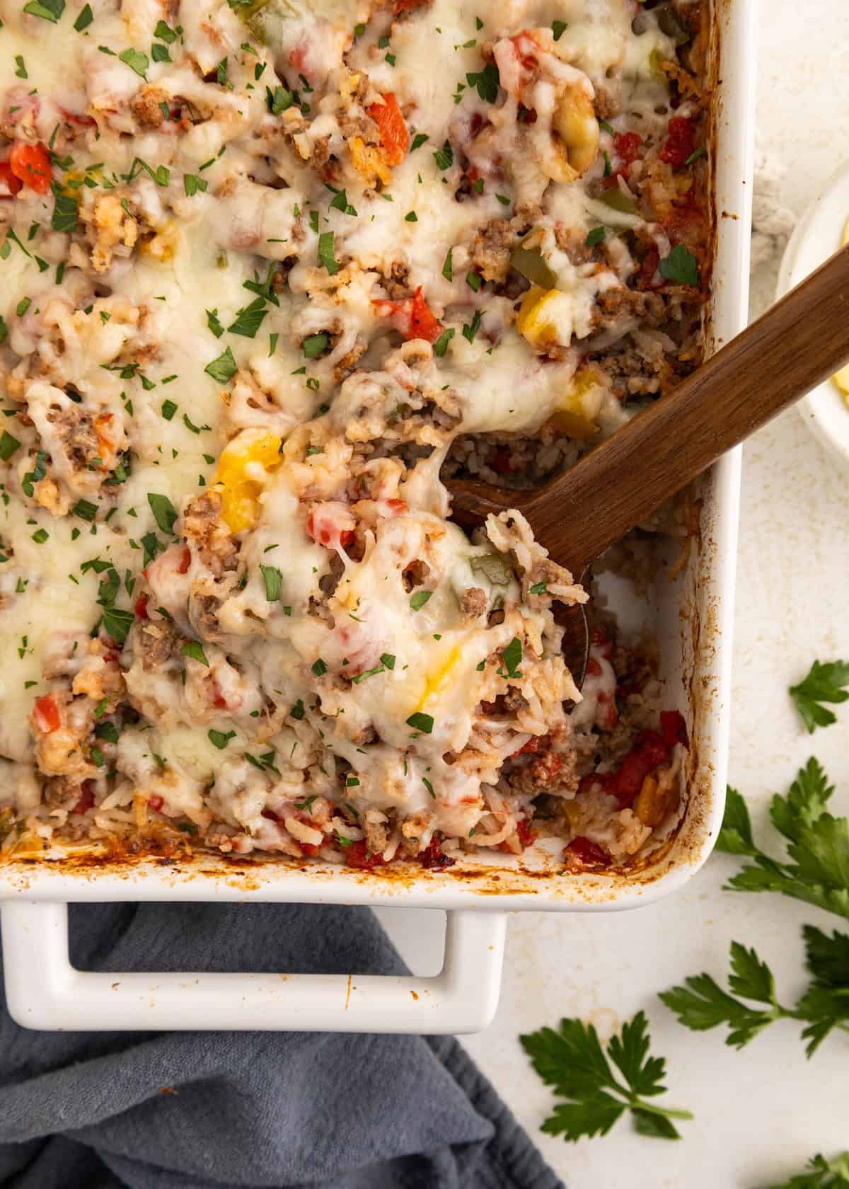 A cheesy baked casserole with ground meat, peppers, and herbs in a white dish.
