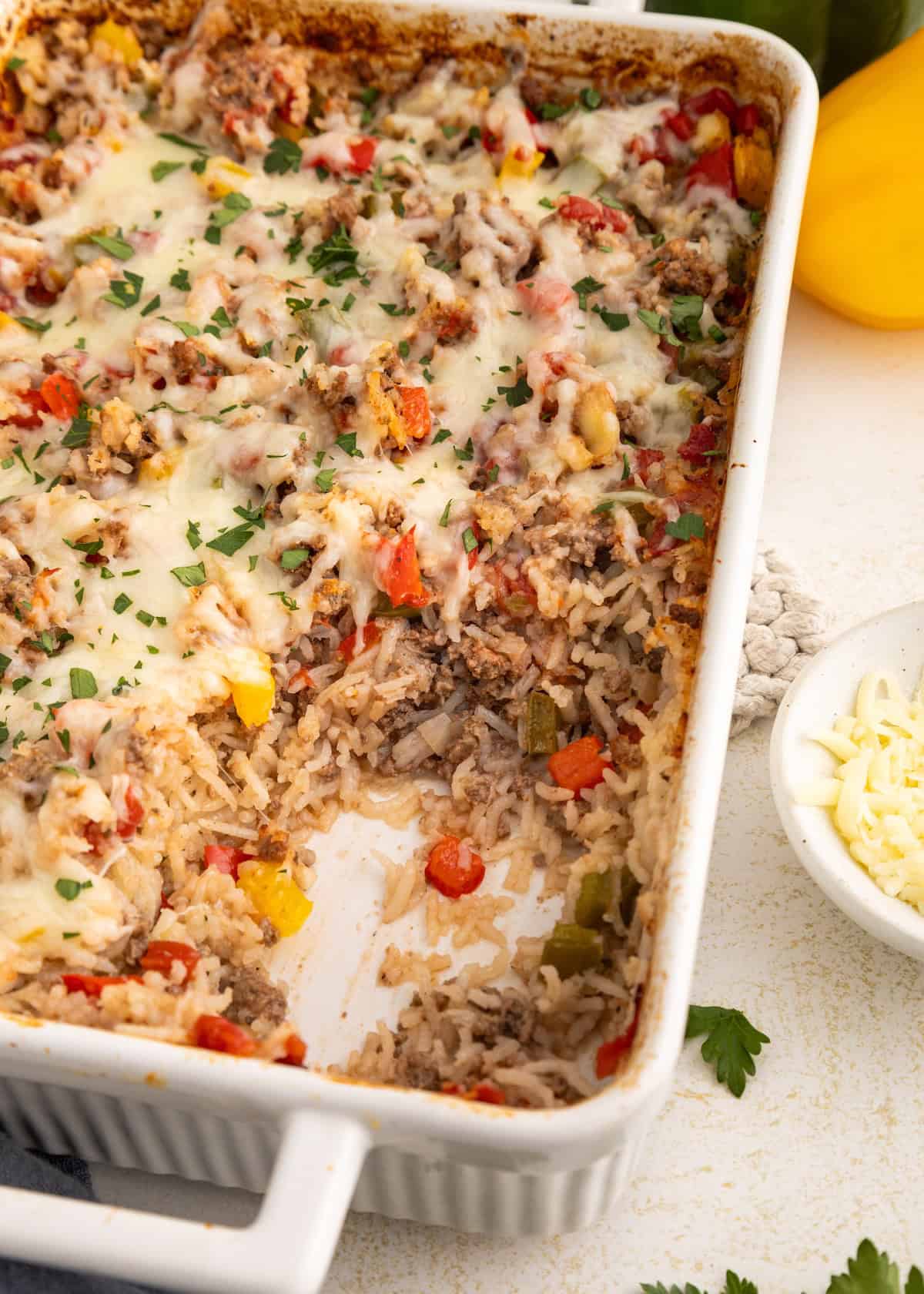 Casserole dish with baked rice, ground meat, bell peppers, and melted cheese, partially served.
