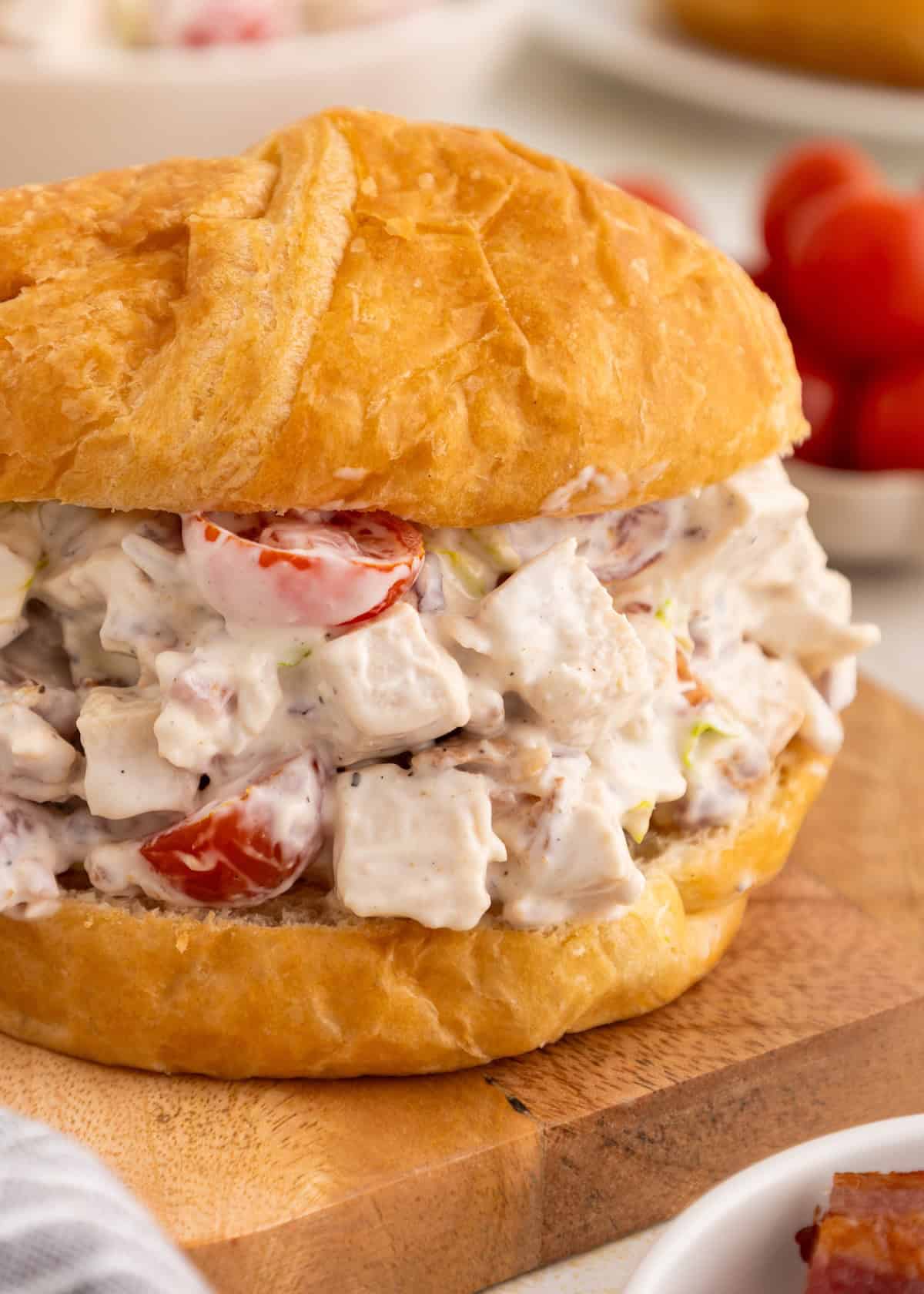 Chicken salad sandwich with diced tomatoes and creamy dressing on a golden bun, close up.