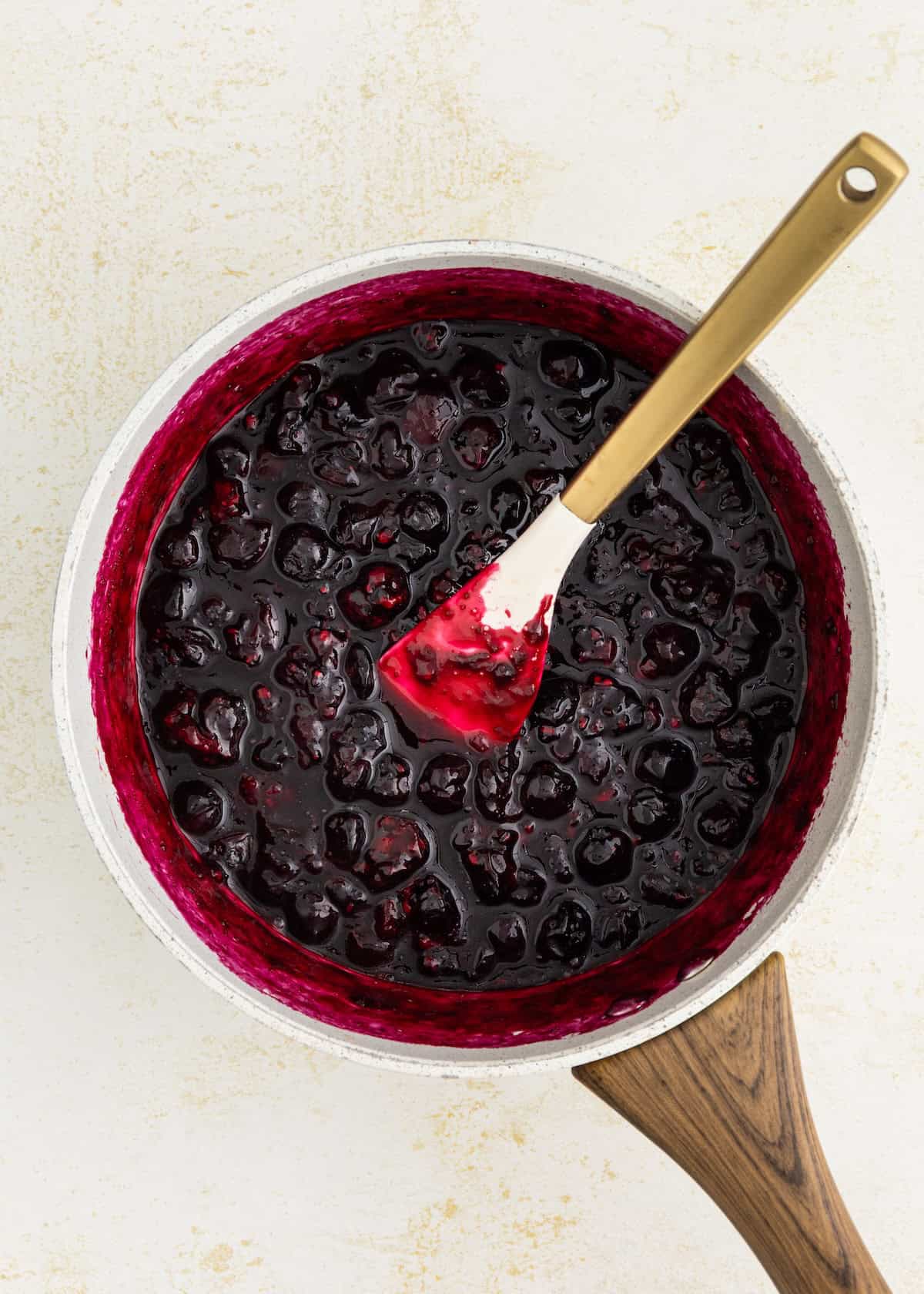 A saucepan of blueberry sauce with a spatula resting inside.