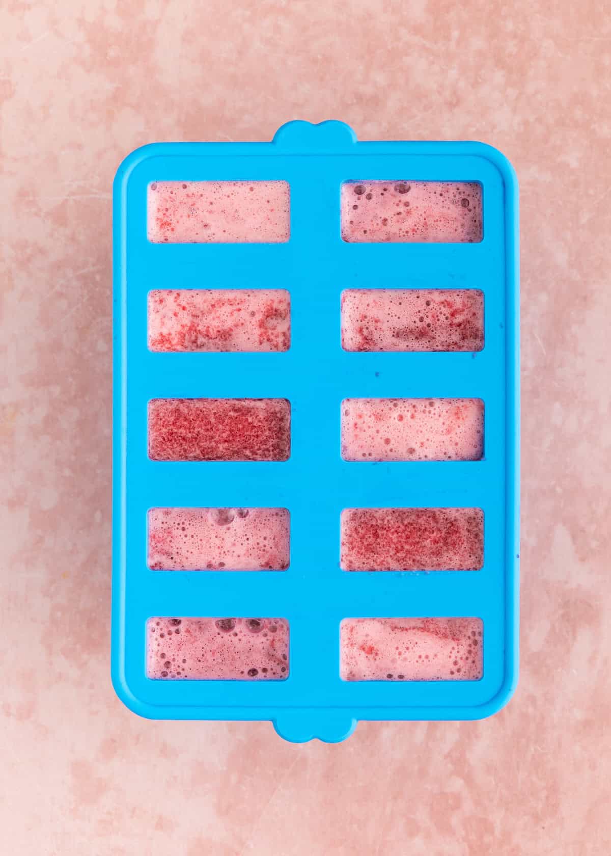 Blue silicone ice tray filled with a pink and purple liquid mixture, on a light surface.