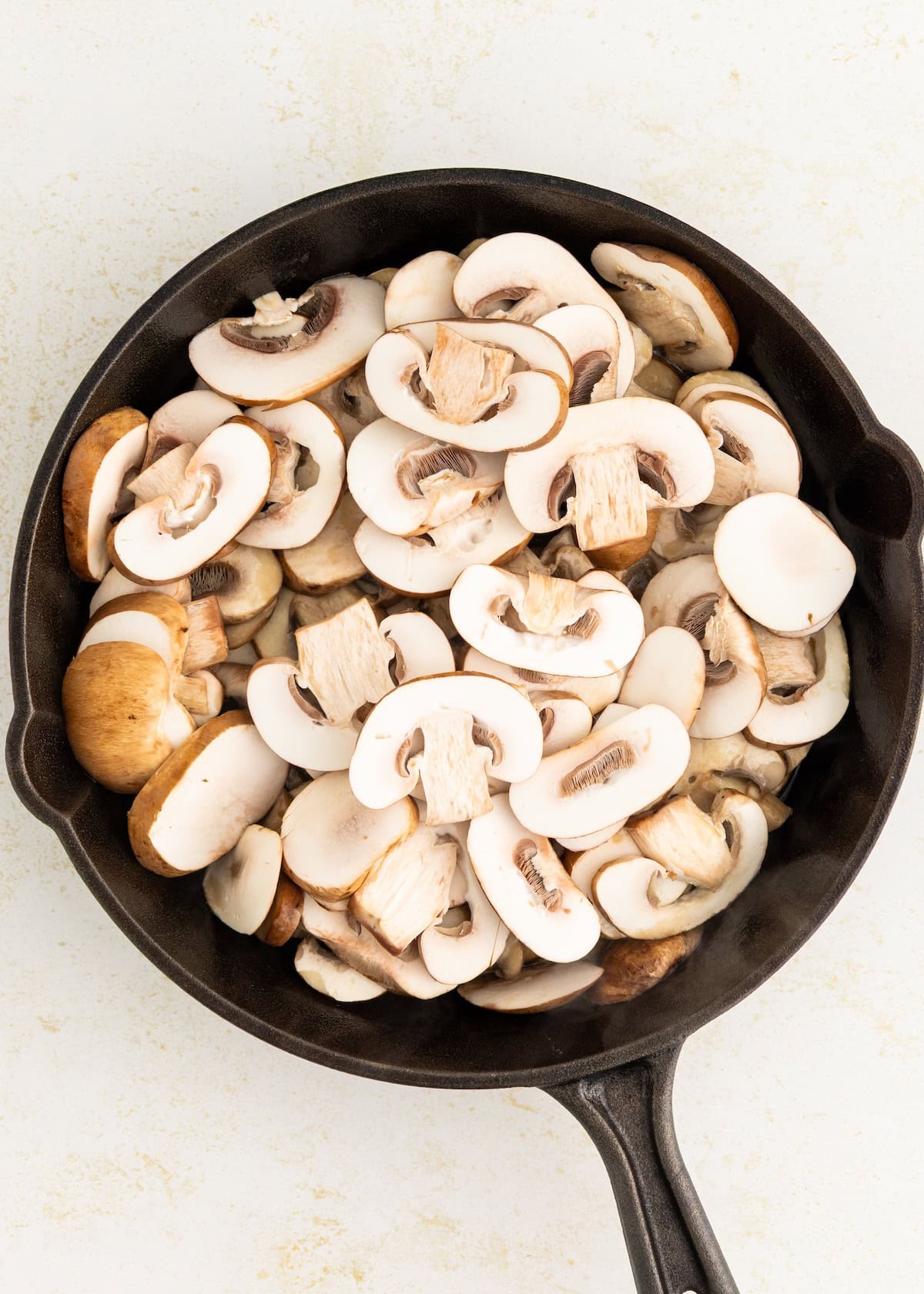 Sliced mushrooms in a black skillet on a light-colored surface.