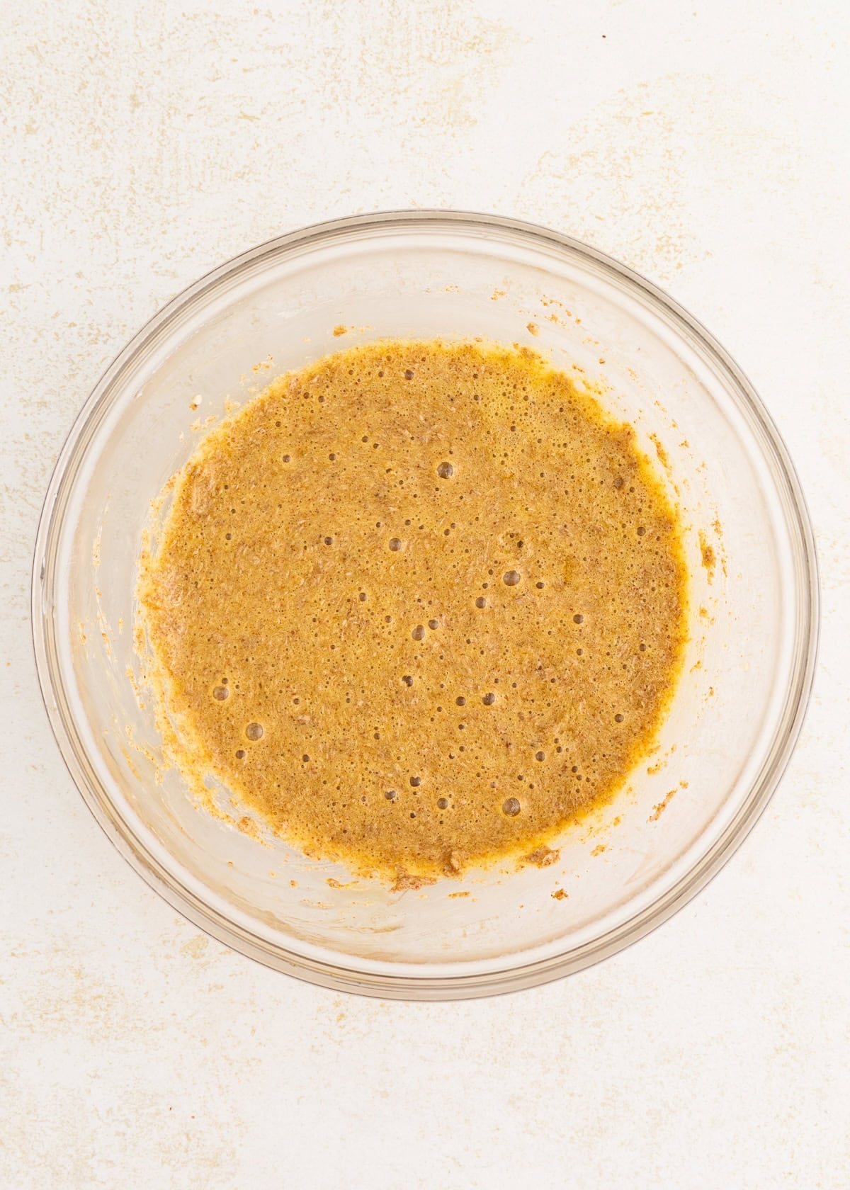 Glass bowl with a bubbly, brown batter mixture on a light-colored surface.