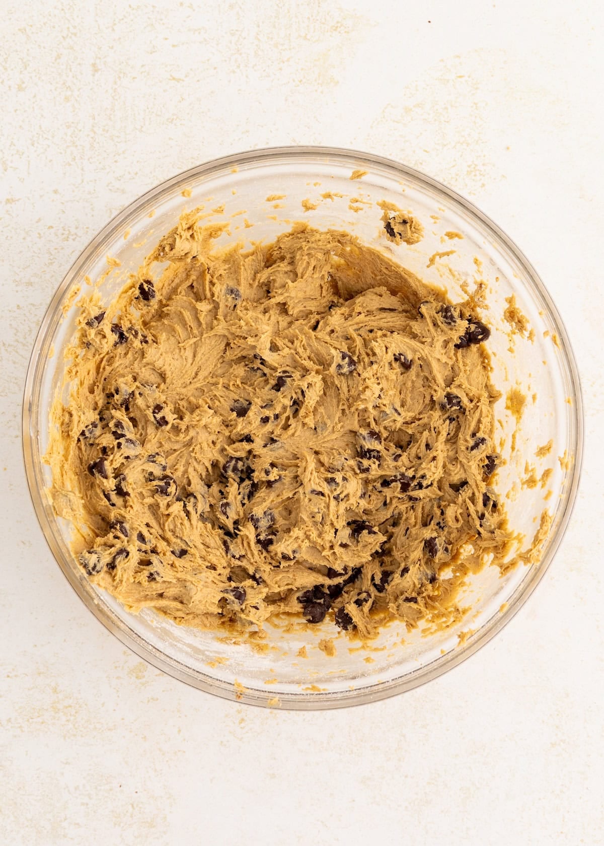 Glass bowl filled with chocolate chip cookie dough on a light surface.