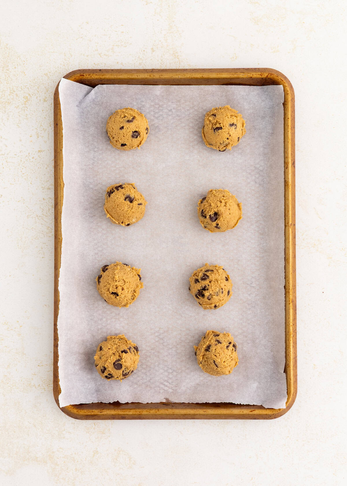 Eight chocolate chip cookie dough balls on a parchment-lined baking sheet.