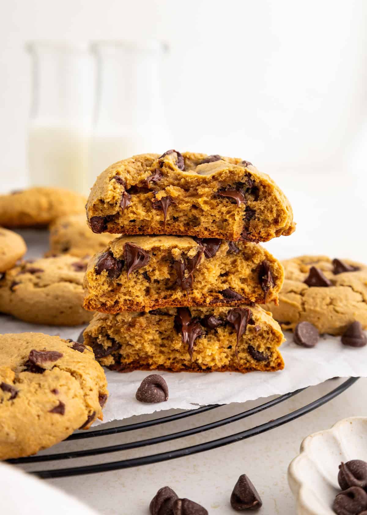 These are thick, soft chocolate chip cookies with melty chips, stacked on a rack with milk in back.