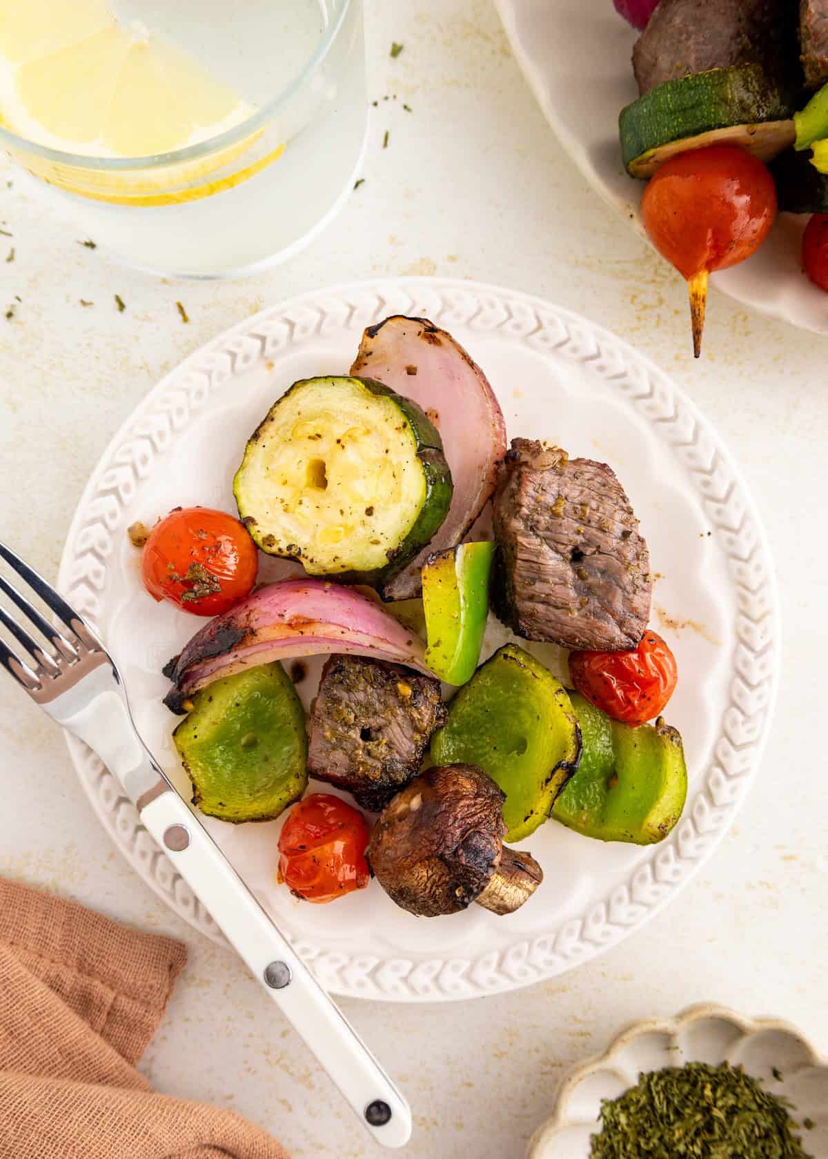 Plate with grilled steak, zucchini, bell pepper, onion, tomato, and mushroom, plus a fork.