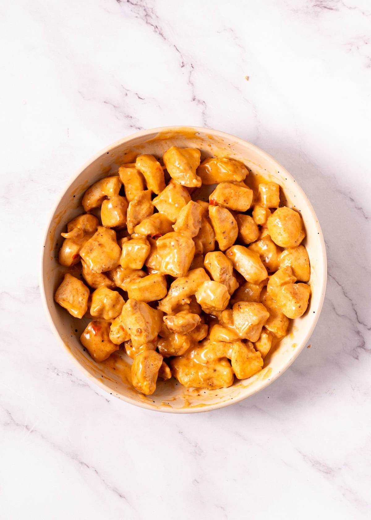 Bowl of marinated chicken pieces on a white marble surface.