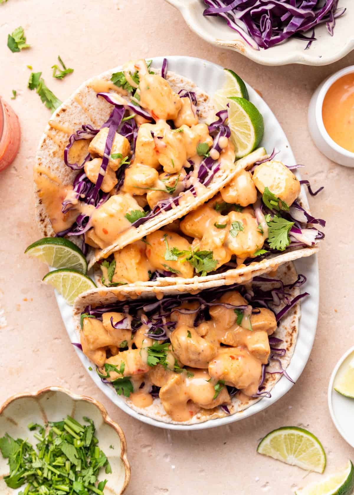 Three tacos filled with diced chicken, purple cabbage, creamy sauce, cilantro, and lime wedges.