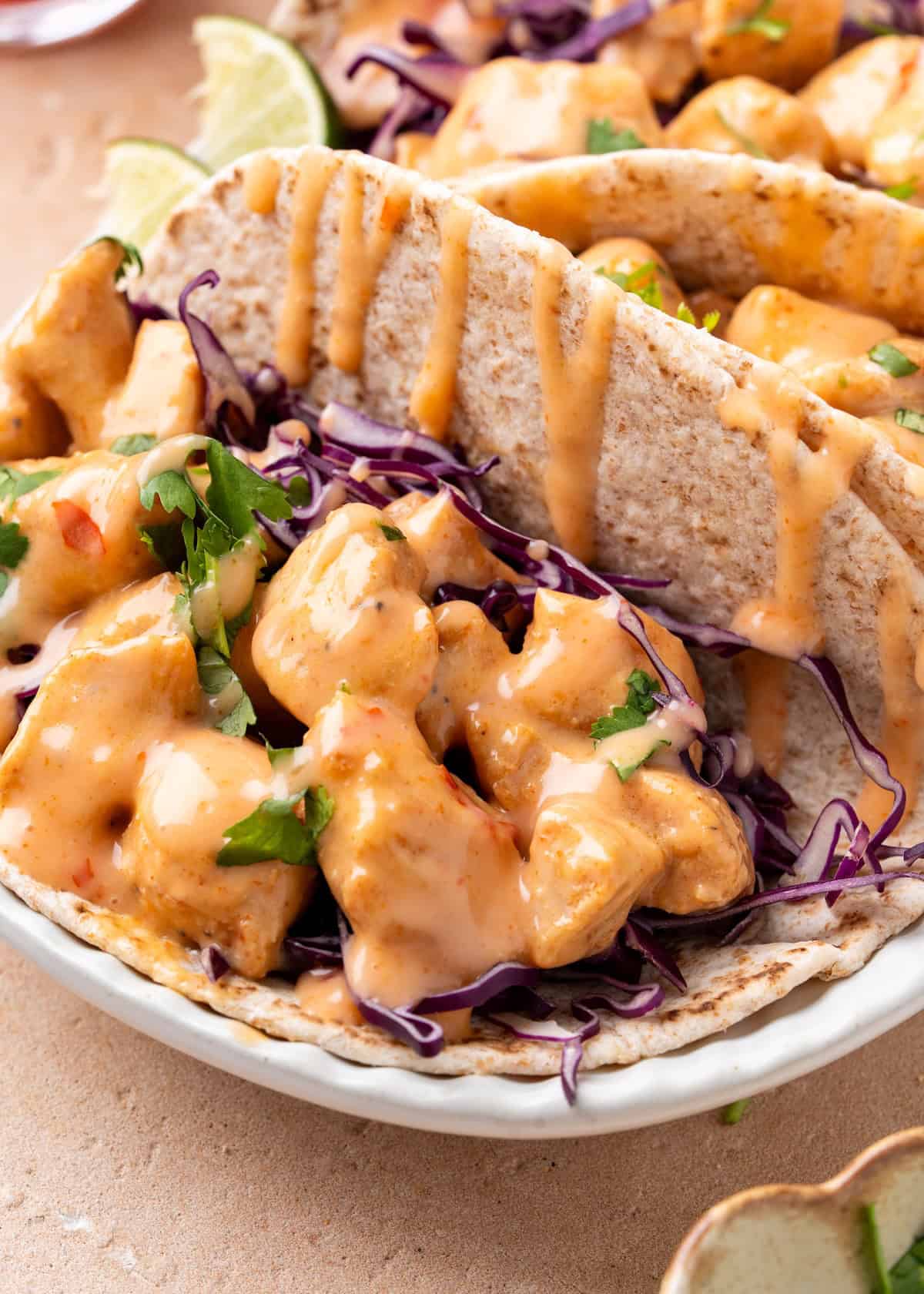 Soft taco with saucy chicken, shredded purple cabbage, cilantro, and lime wedge in background.