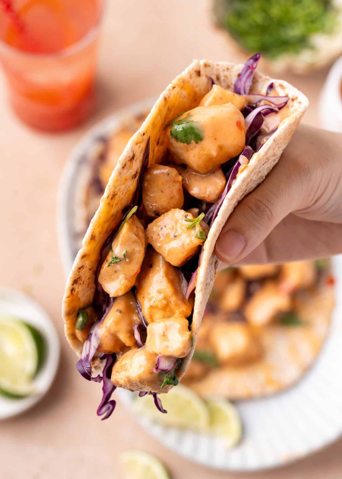 Hand holding a taco filled with saucy chicken, purple cabbage, and herbs.