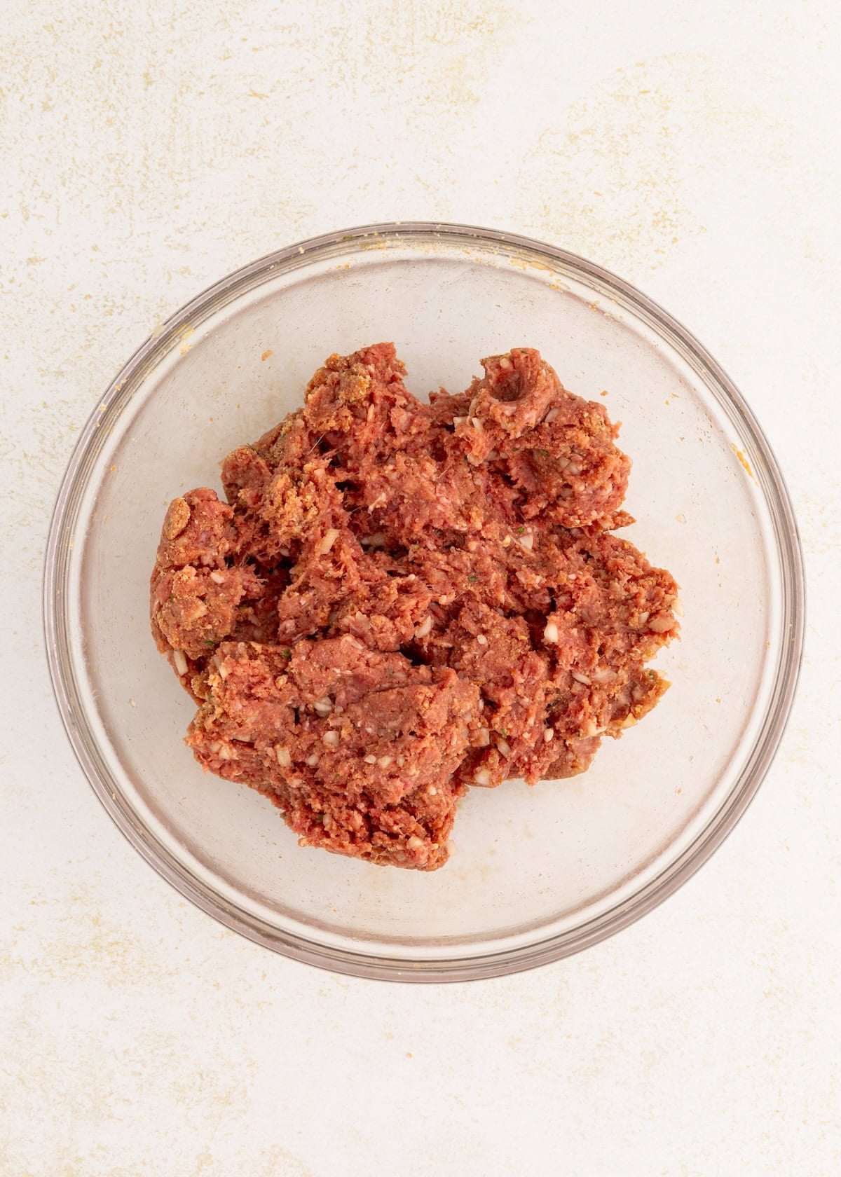 Ground meat mixture for Salisbury Steak with Mushroom Gravy in a clear bowl on a light surface.