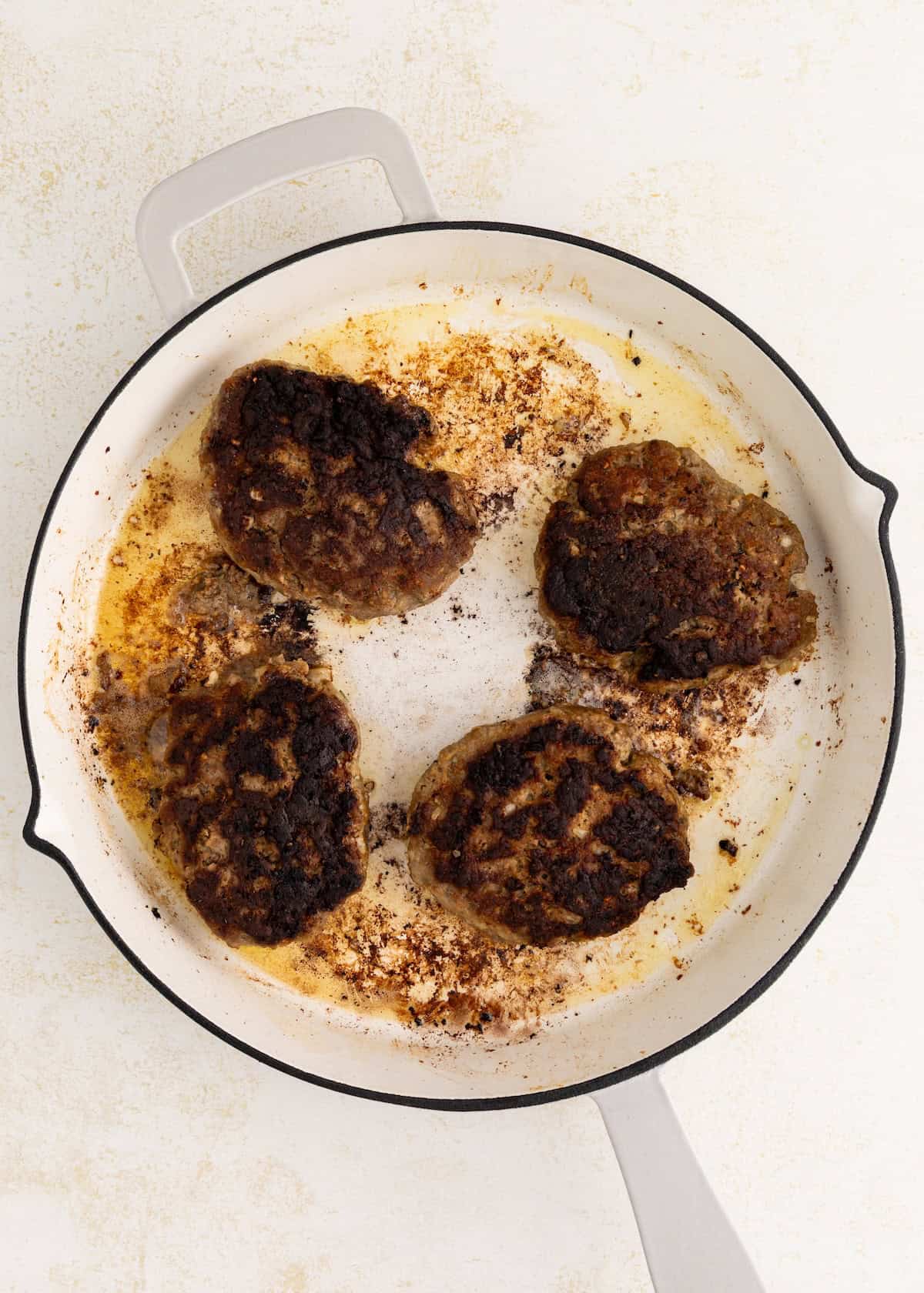 Four burnt Salisbury Steak with Mushroom Gravy patties in a white skillet with burnt residue.