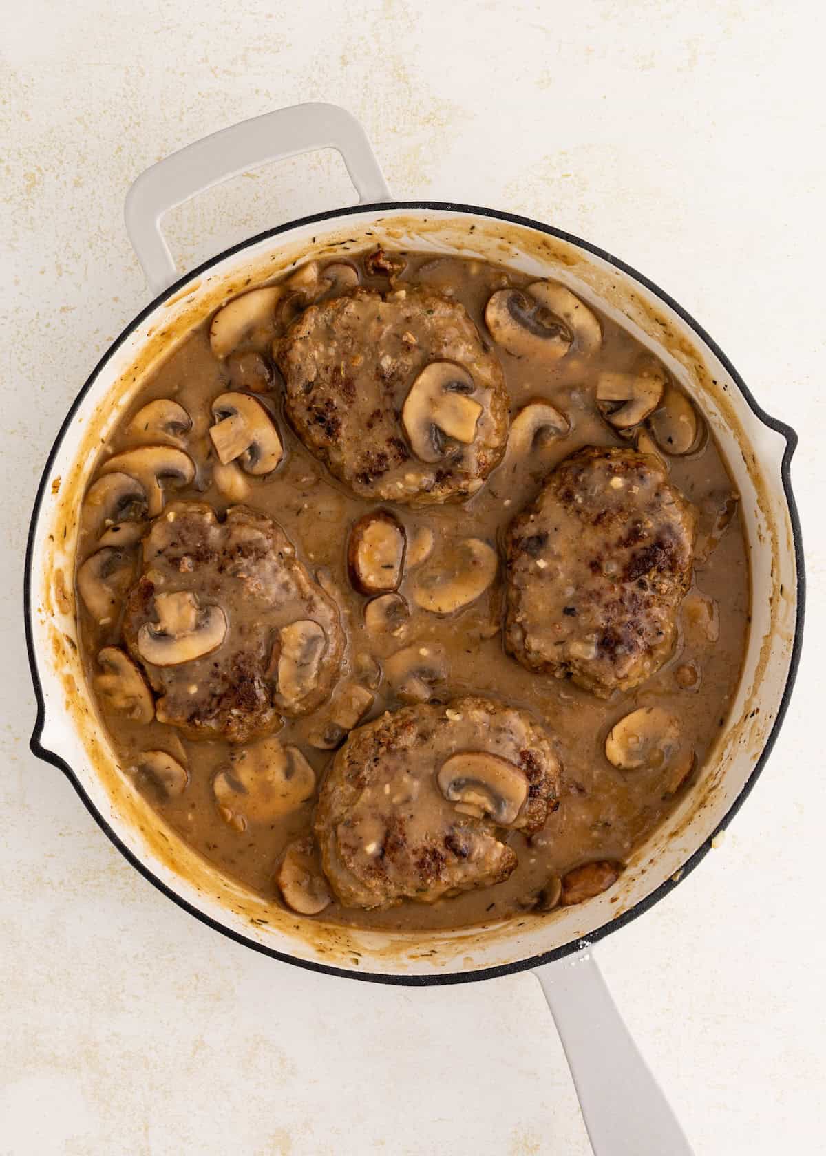 Salisbury Steak with Mushroom Gravy, four servings in a white skillet, viewed from above.