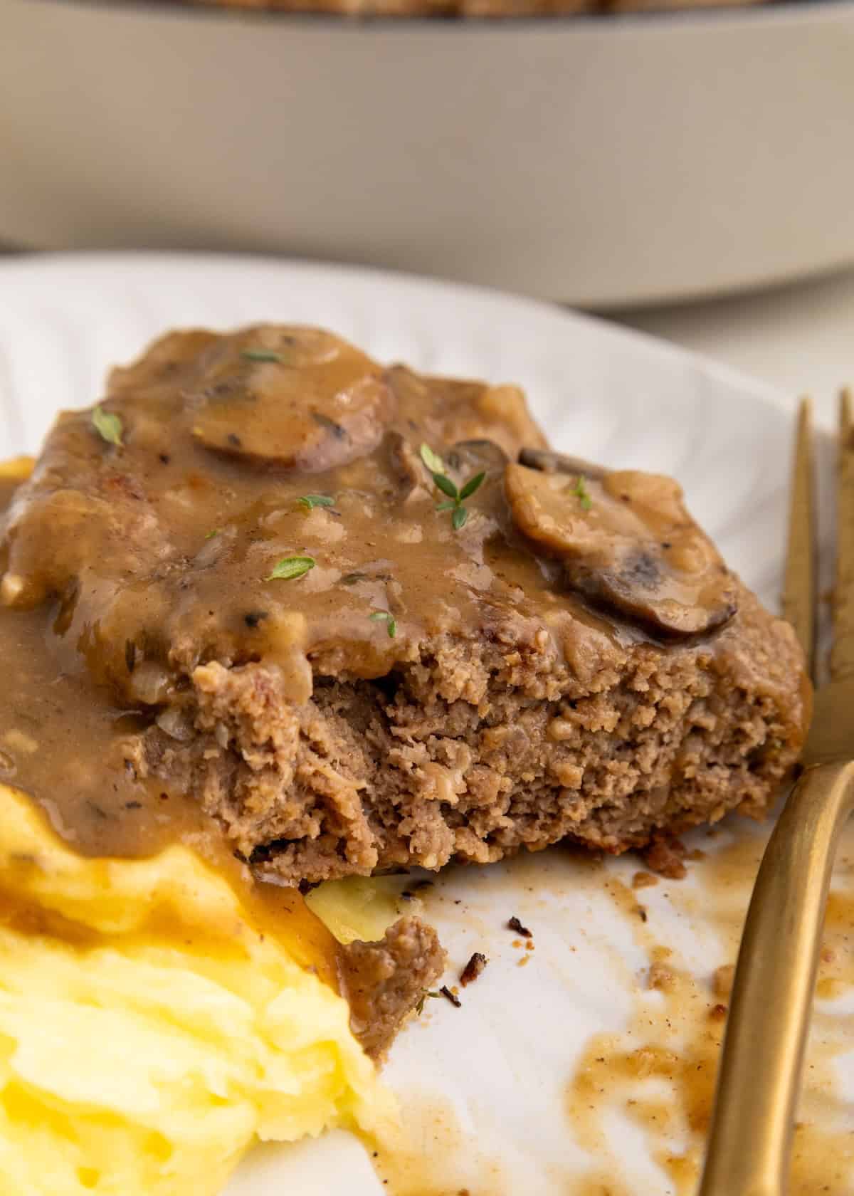 Enjoy Salisbury Steak with Mushroom Gravy served alongside mashed potatoes on a white plate.