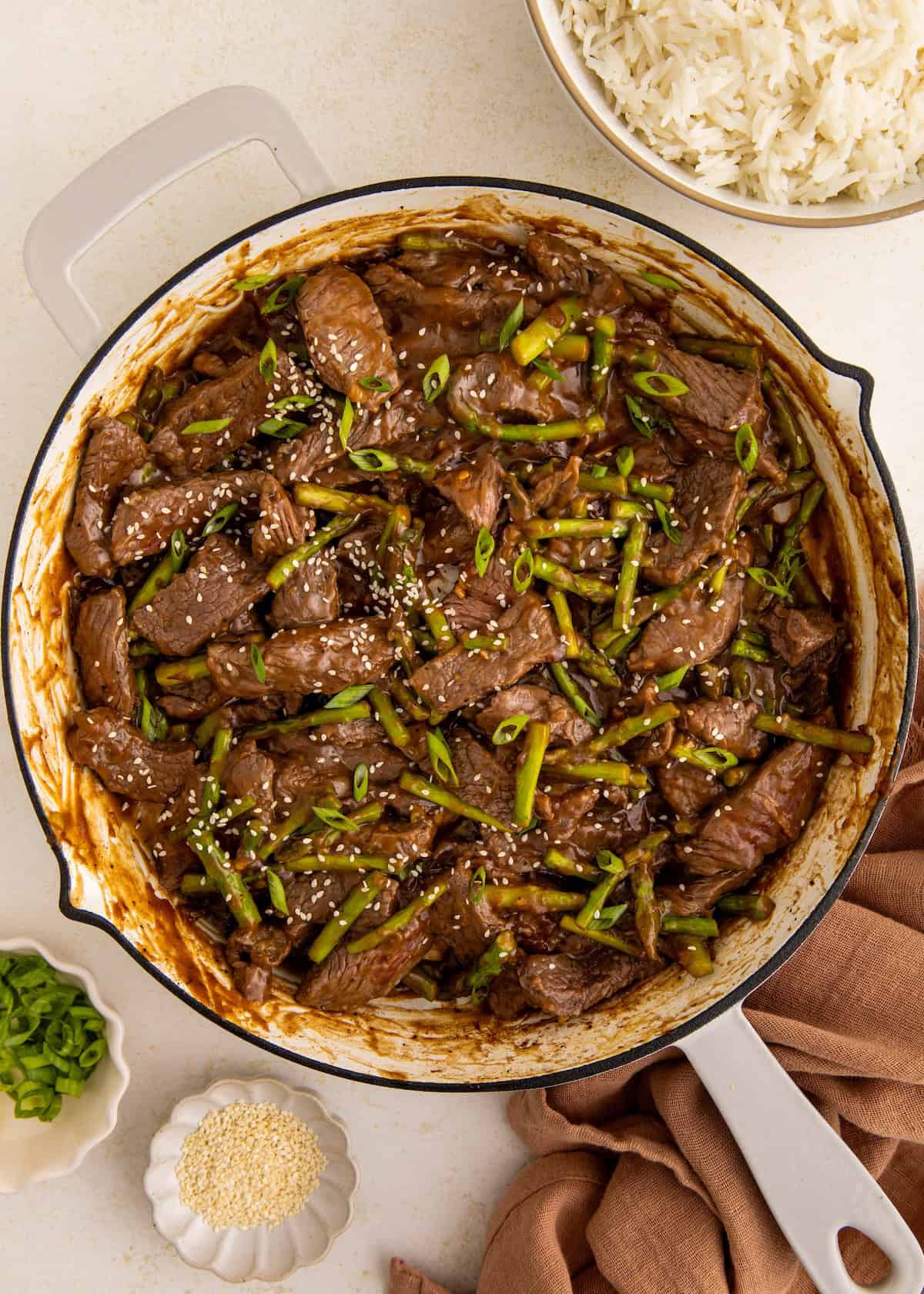Beef stir fry with green beans in a skillet, topped with sesame seeds and green onions.