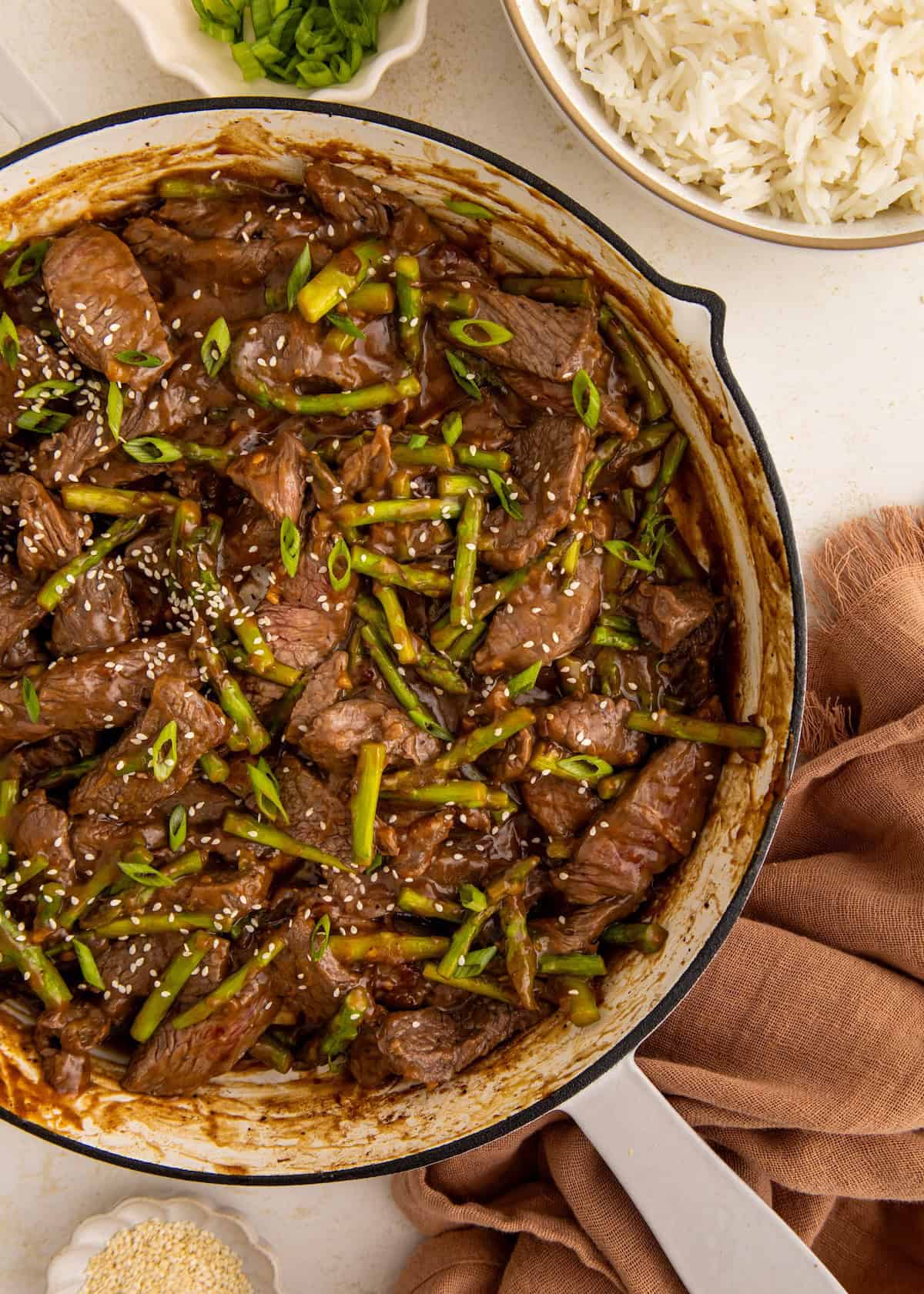 Beef stir-fry with green beans and sesame seeds in a pan, served with rice and green onions.
