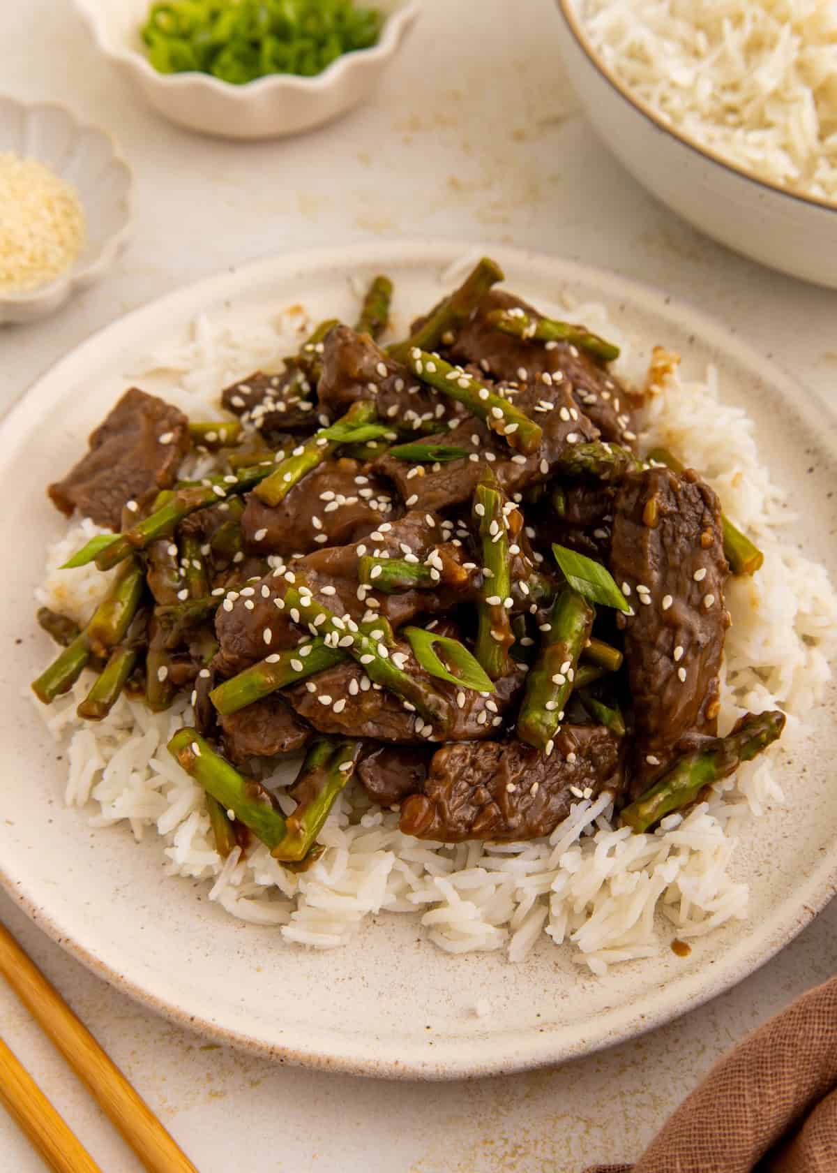 Beef and asparagus stir-fry on white rice, topped with sesame seeds on a plate.