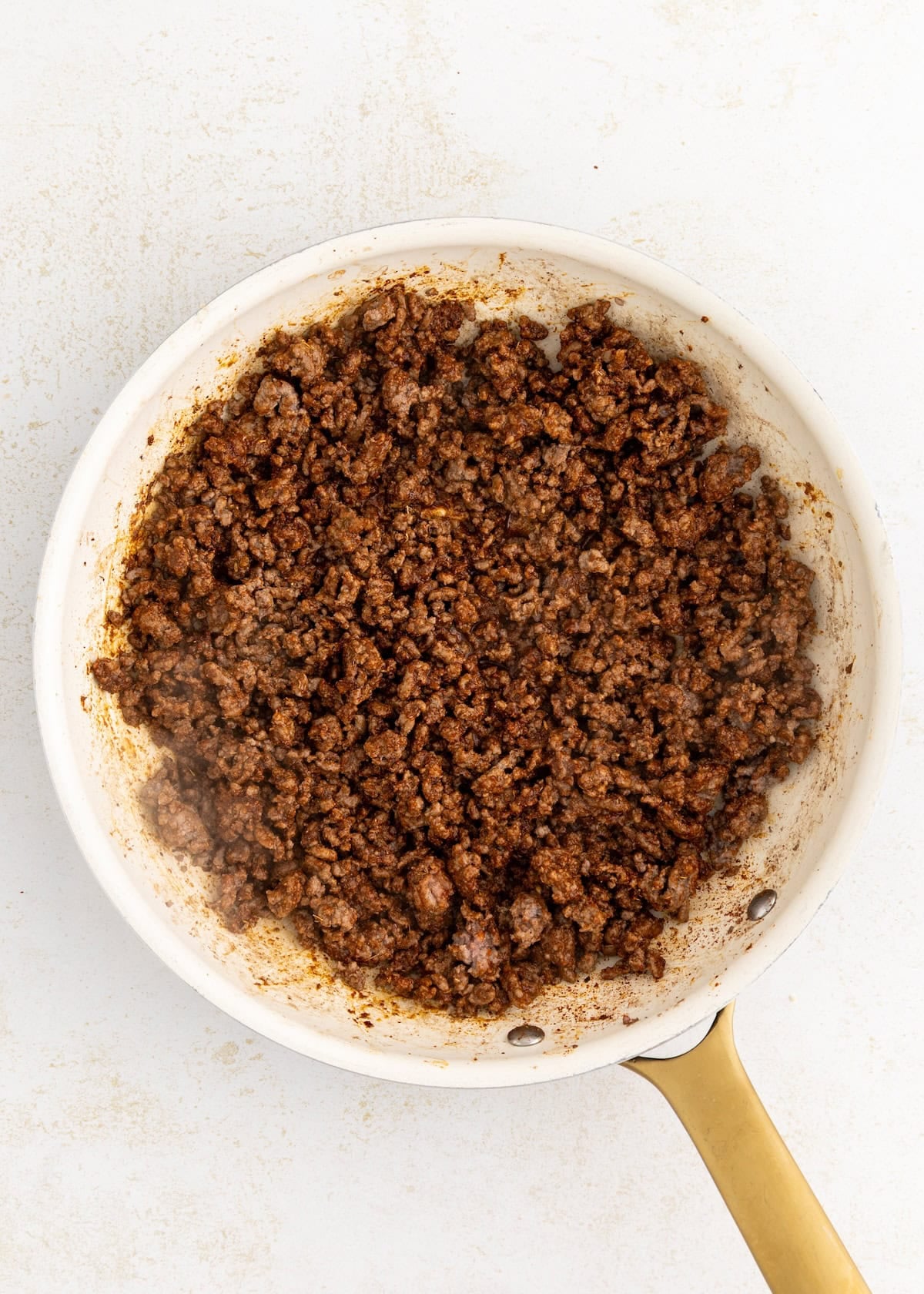 Cooked ground beef with spices in a white skillet on a light countertop.