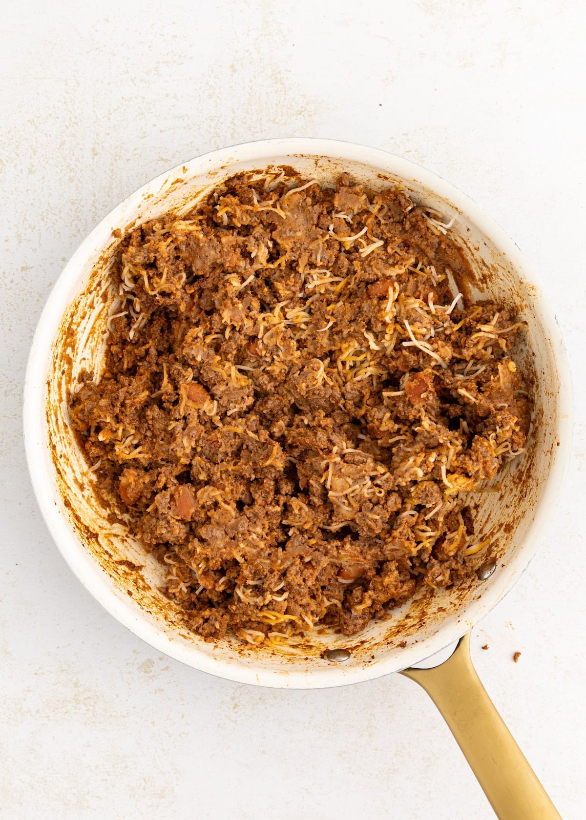 Shredded chicken and spices mixed in a white skillet with a gold handle.