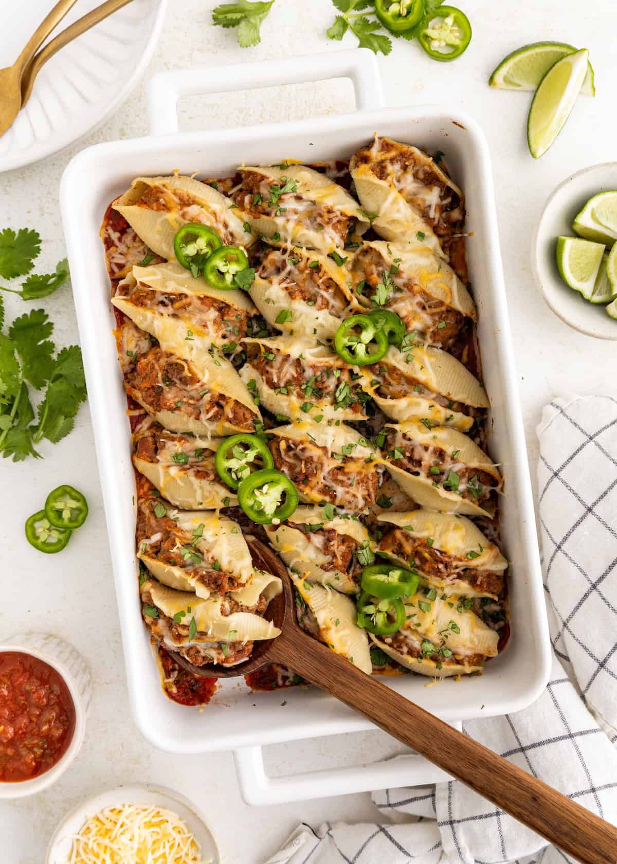 Stuffed pasta shells topped with melted cheese and sliced jalapeños in a white baking dish.