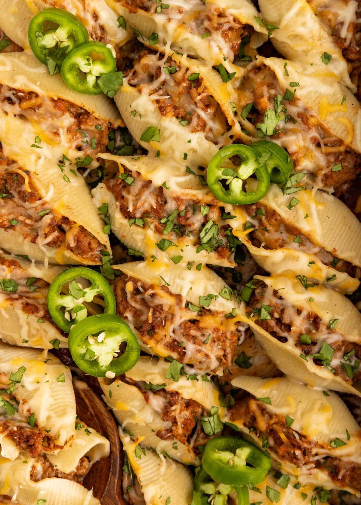 Stuffed pasta shells with melted cheese, ground meat, and sliced jalapeños, garnished with herbs.