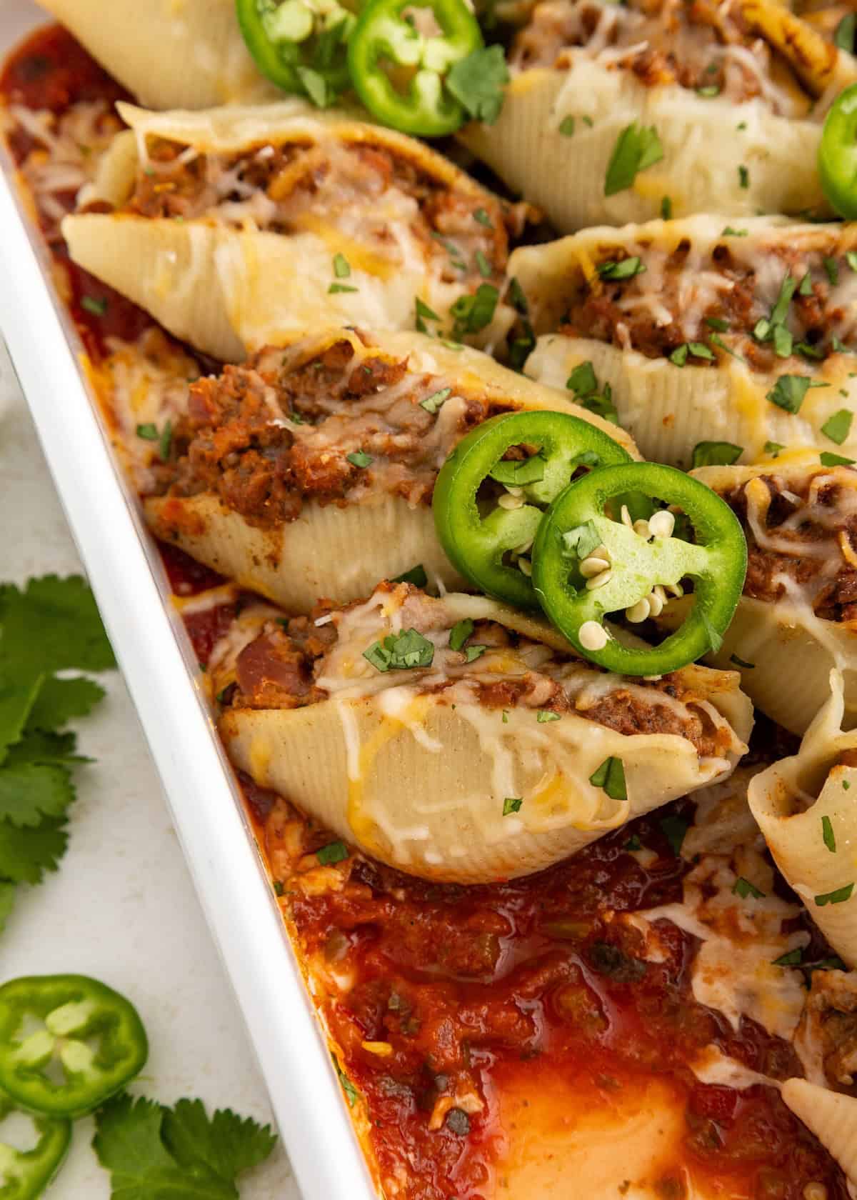 Stuffed pasta shells with meat, cheese, jalapeños, and sauce in a baking dish, garnished with herbs.