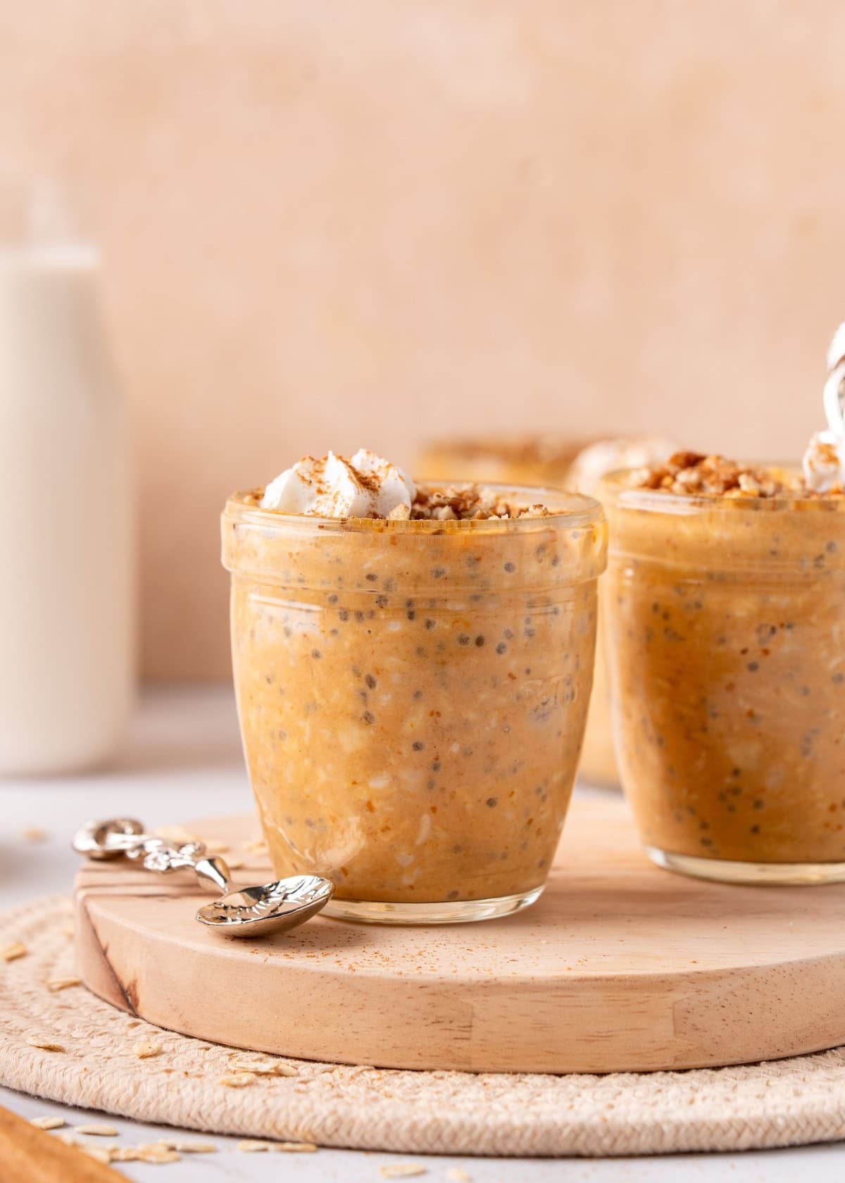 Pumpkin chia pudding in glass jars, topped with granola and whipped cream, on a wooden board.