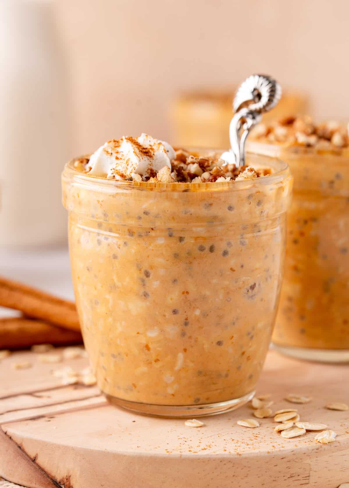 A jar of pumpkin overnight oats topped with whipped cream and granola on a wooden board.