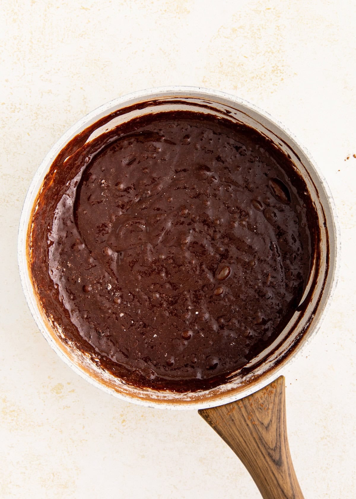 Bowl of chocolate brownie batter with a wooden handle on a light background.