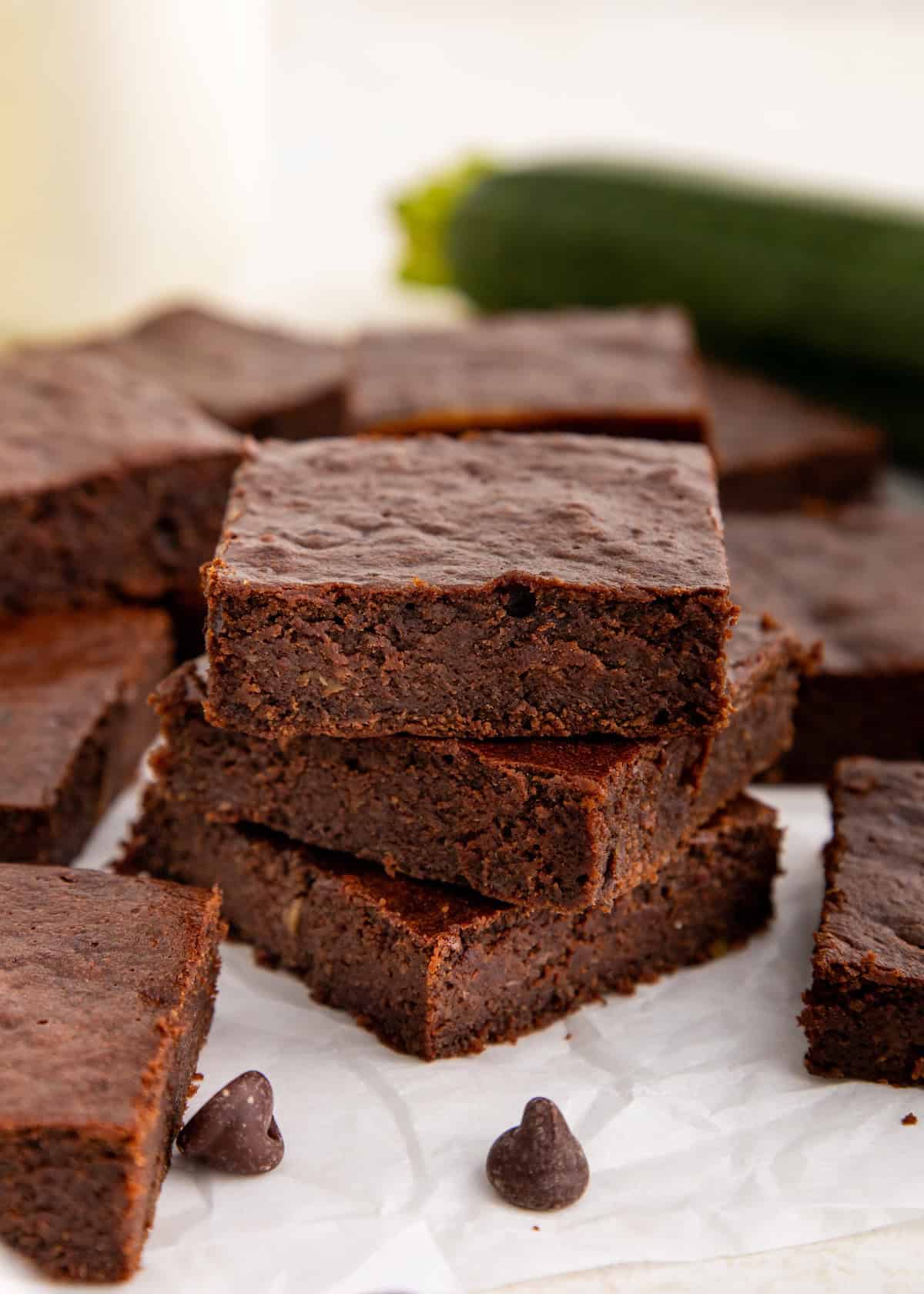 A stack of chocolate brownies with chocolate chips on parchment paper.