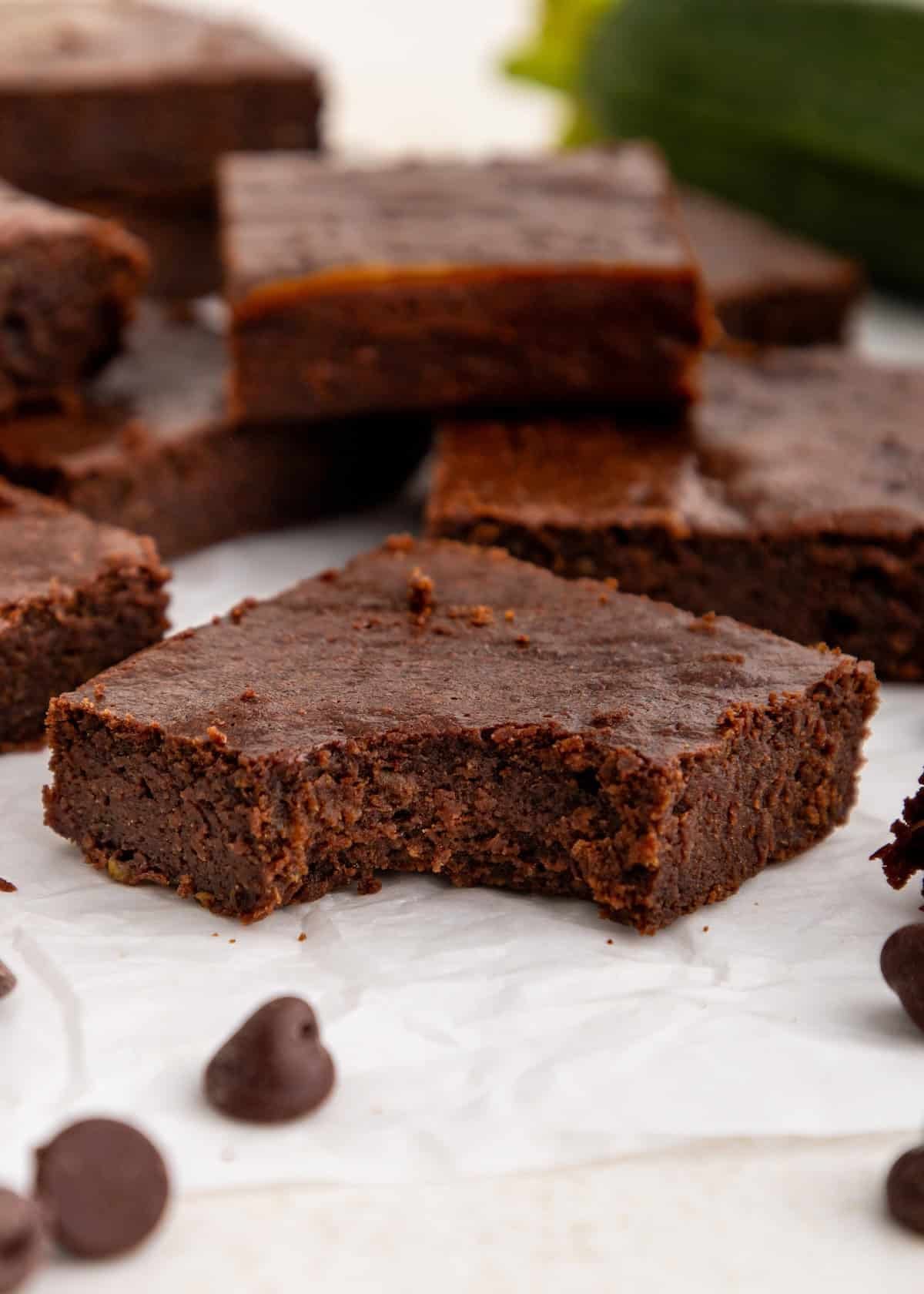 A chocolate brownie with a bite taken out, surrounded by more brownies and chocolate chips.