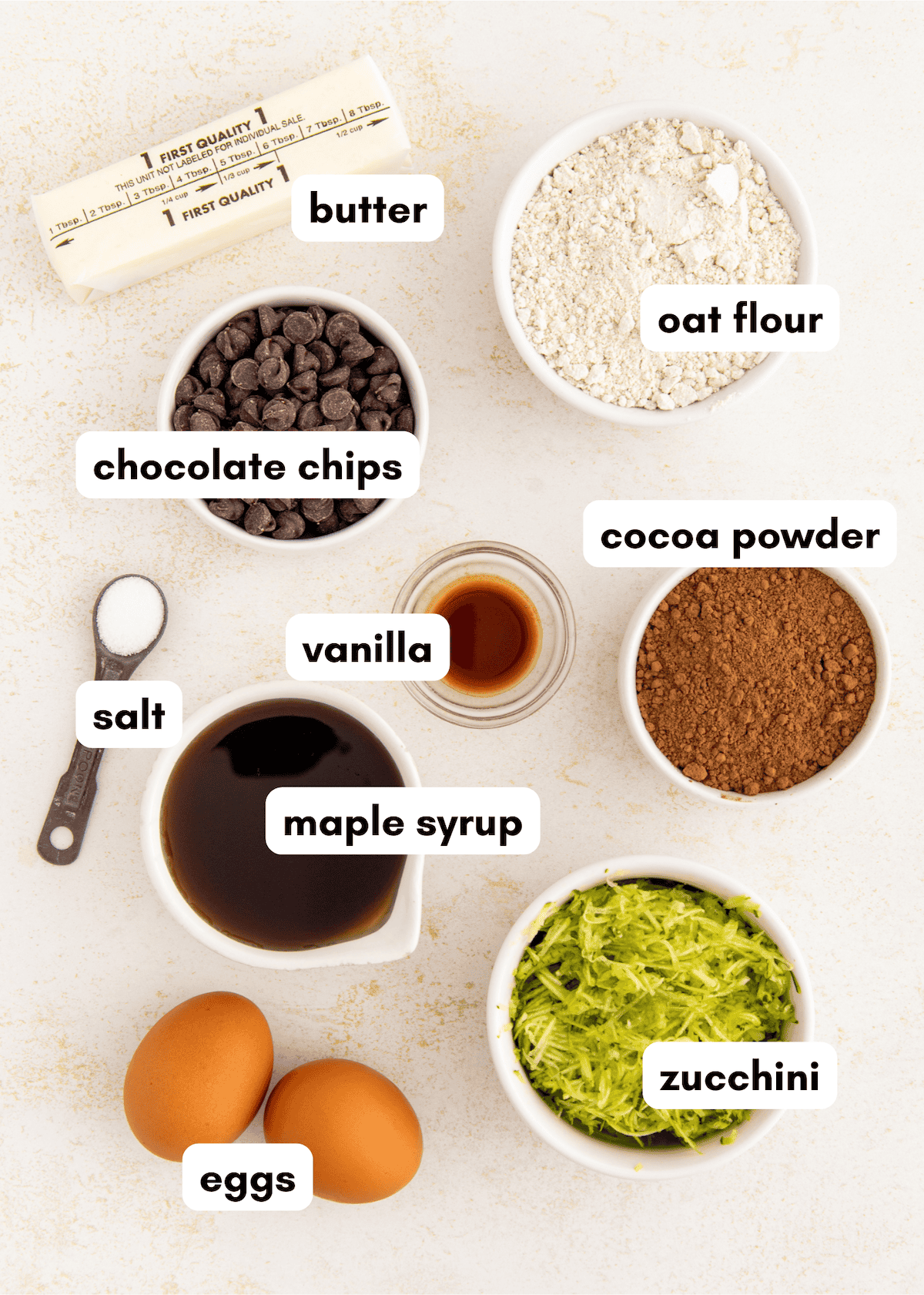 Baking ingredients: butter, oat flour, chocolate chips, cocoa, maple syrup, zucchini, eggs.